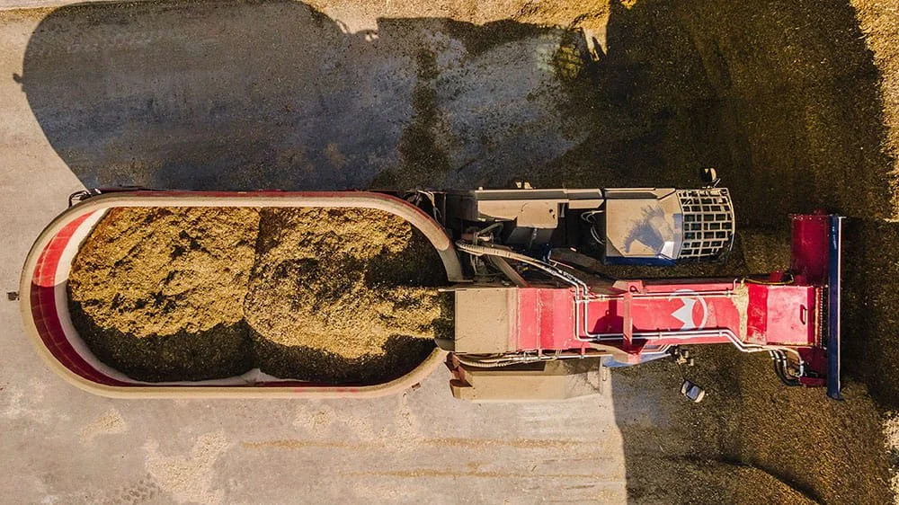 An aerial drone perspective looking down into the open twin-auger mixing tub of a Siloking SelfLine System 300 plus as it blends loaded corn silage rations.