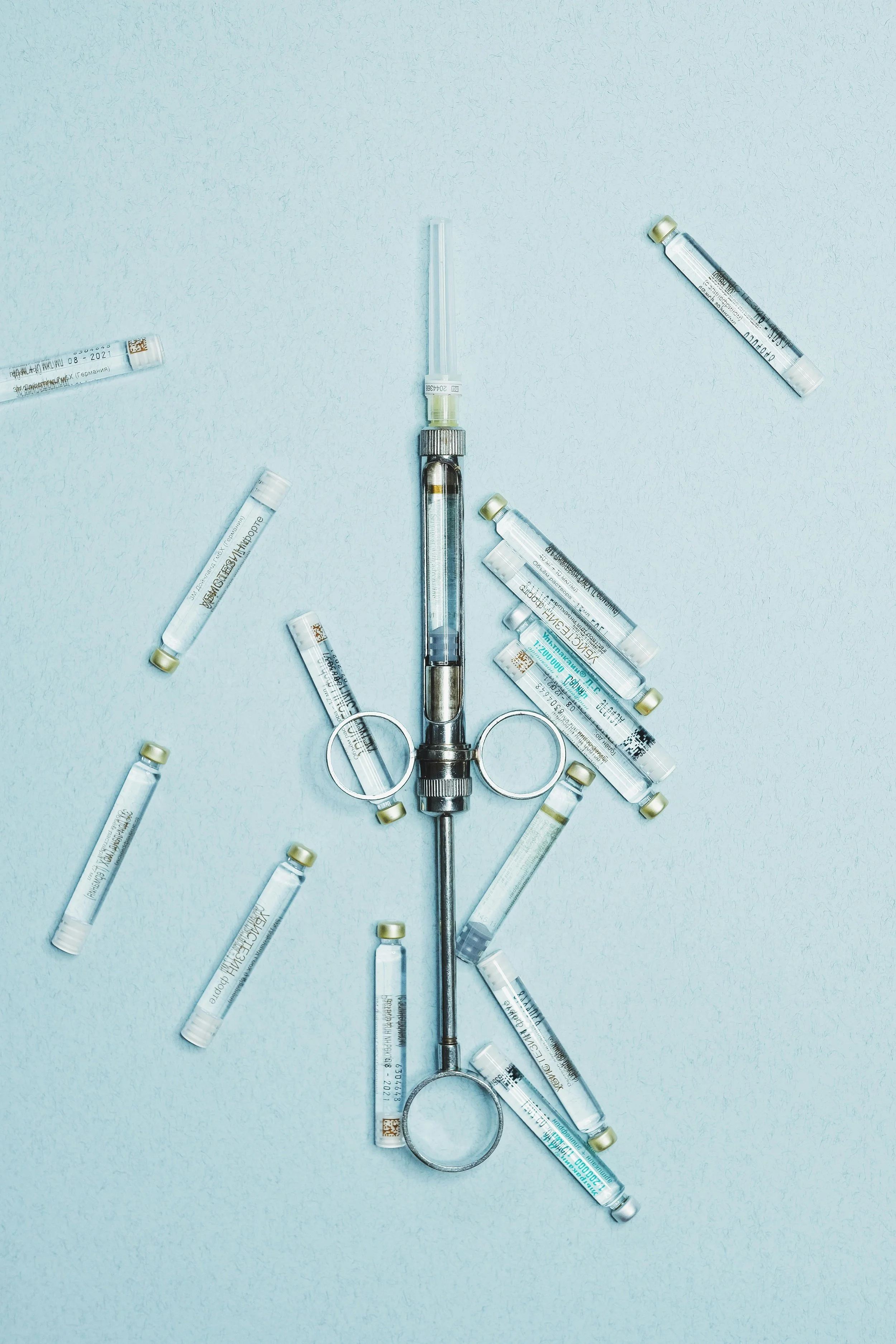 A surgical scalpel with multiple medical ampoules arranged around it on a light blue background.