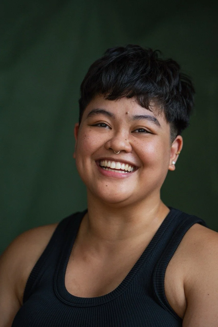 A close-up of a person with short dark hair smiling, wearing a black athletic tank top.