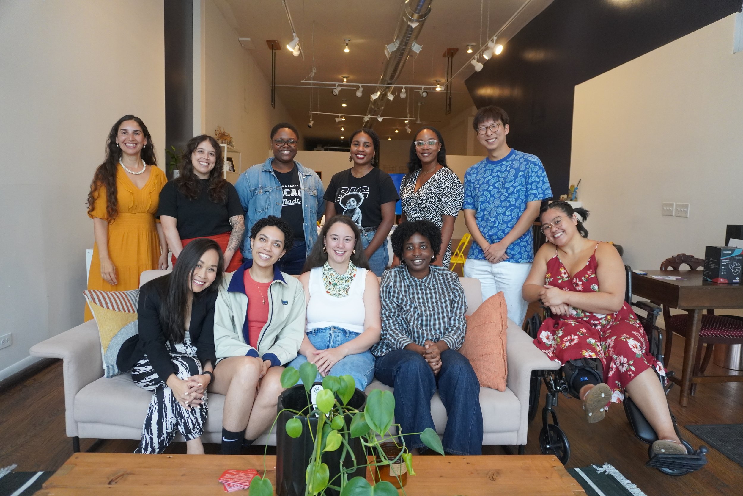 A group of people gathered together in a casual indoor setting, smiling for a photo, with some sitting on a sofa and others standing behind them.