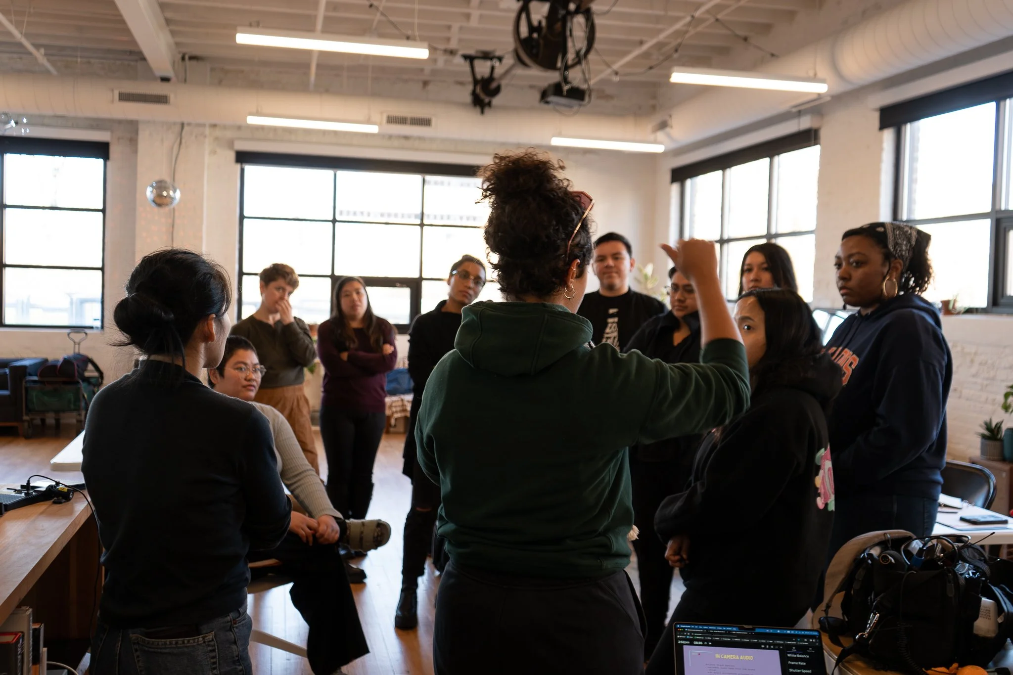 Group of diverse people gathered in a modern indoor space, some seated and others standing, engaged in a discussion.