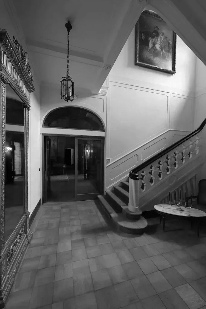 Eleganter Eingangsbereich mit Treppe, Wandbild und antikem Mobiliar in Schwarz-Weiß-Foto.