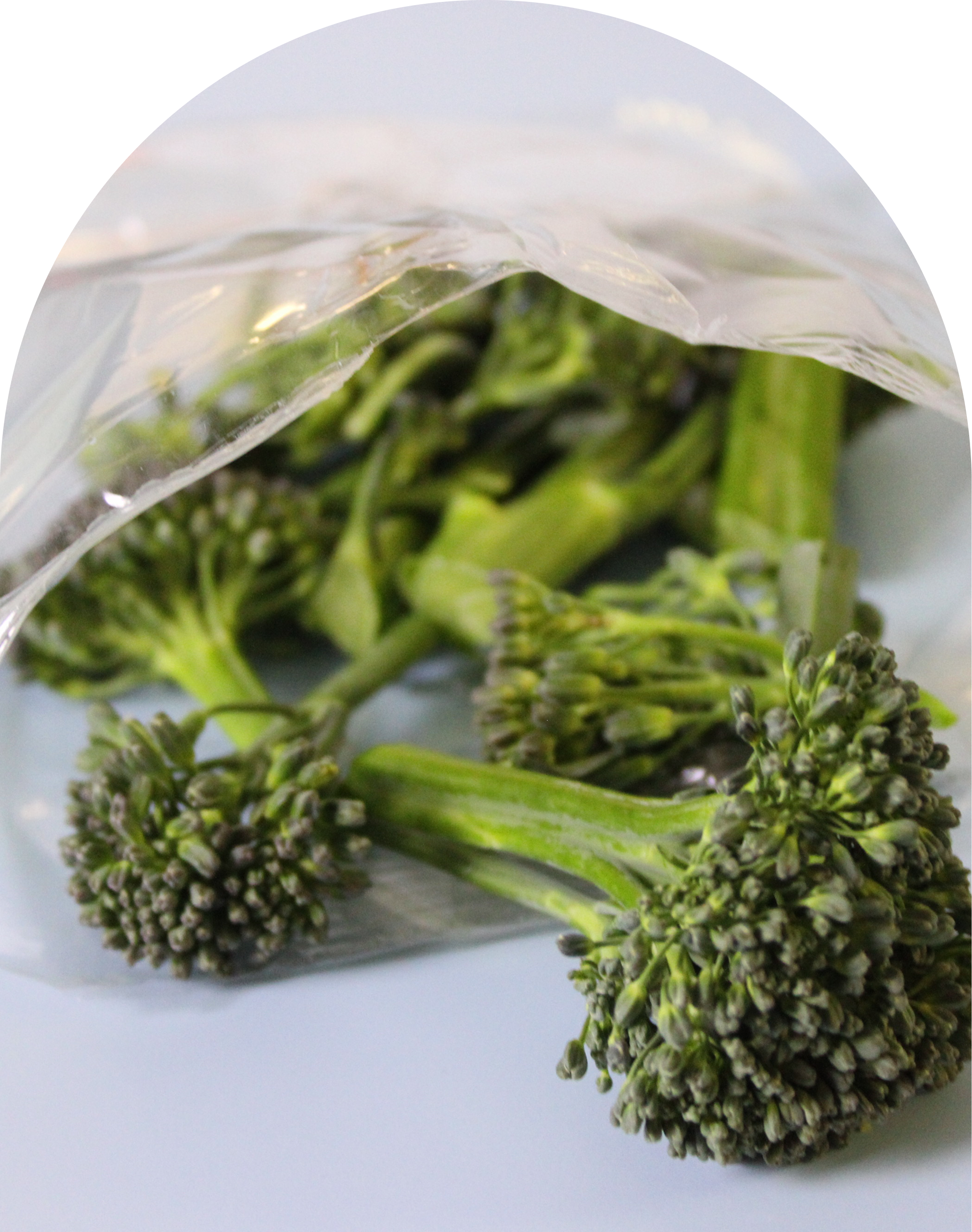 Fresh broccoli florets covered with plastic wrap on a light surface.