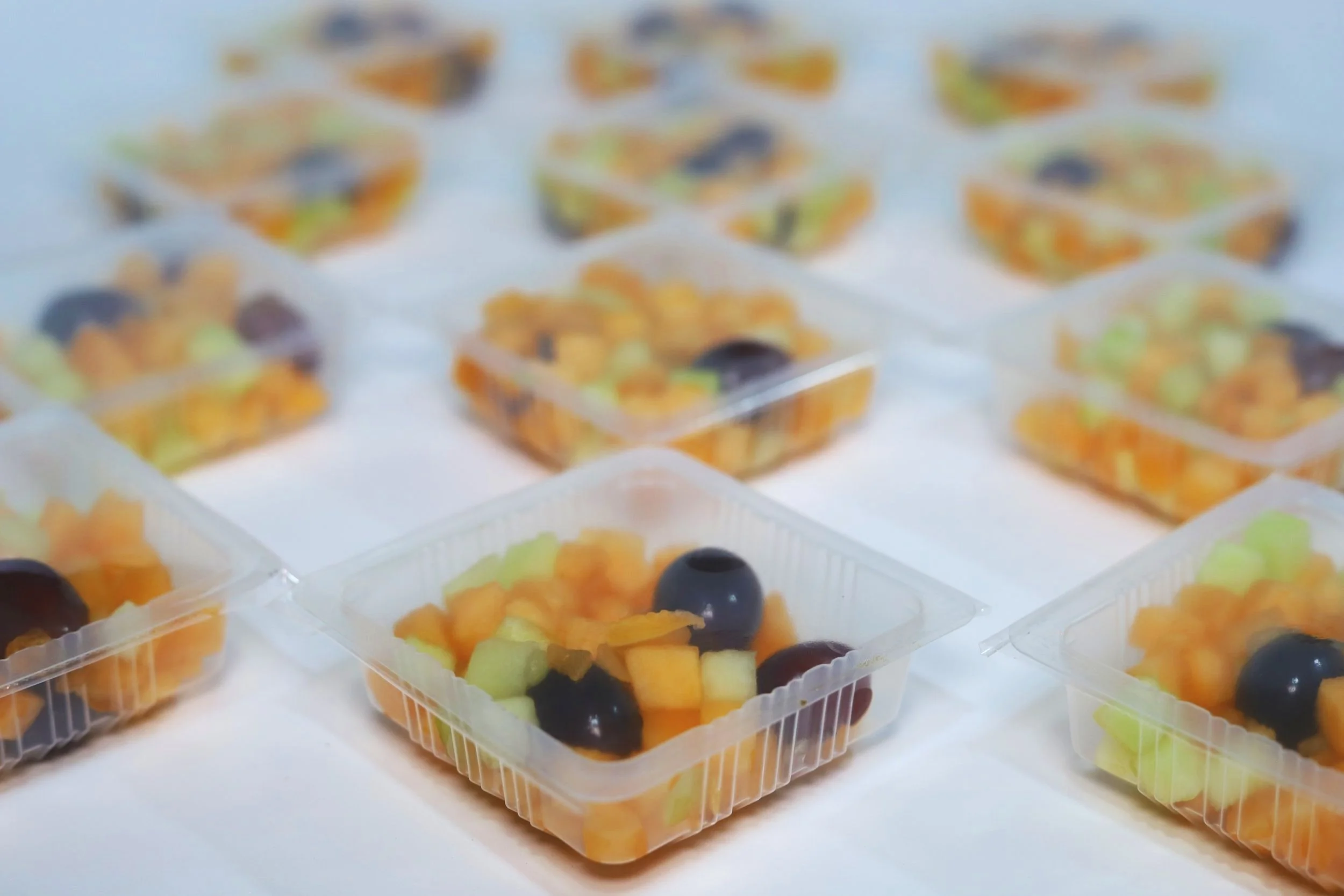 Clear plastic containers filled with cut-up fruit including grapes, melons, and other assorted fruits.