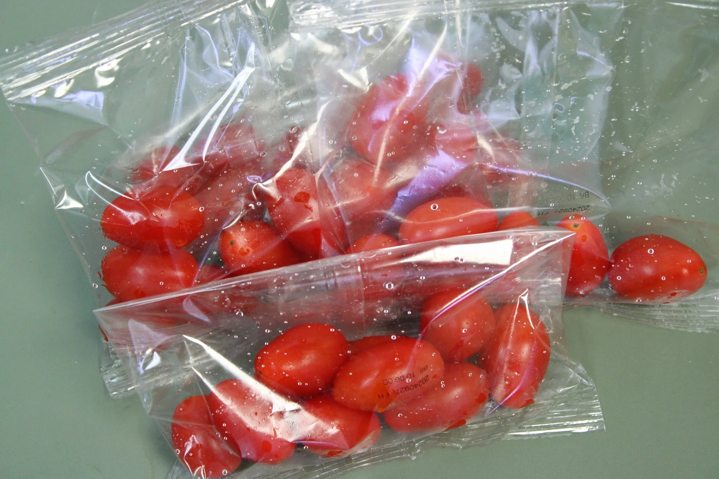 A clear plastic bag filled with cherry tomatoes on a gray surface.