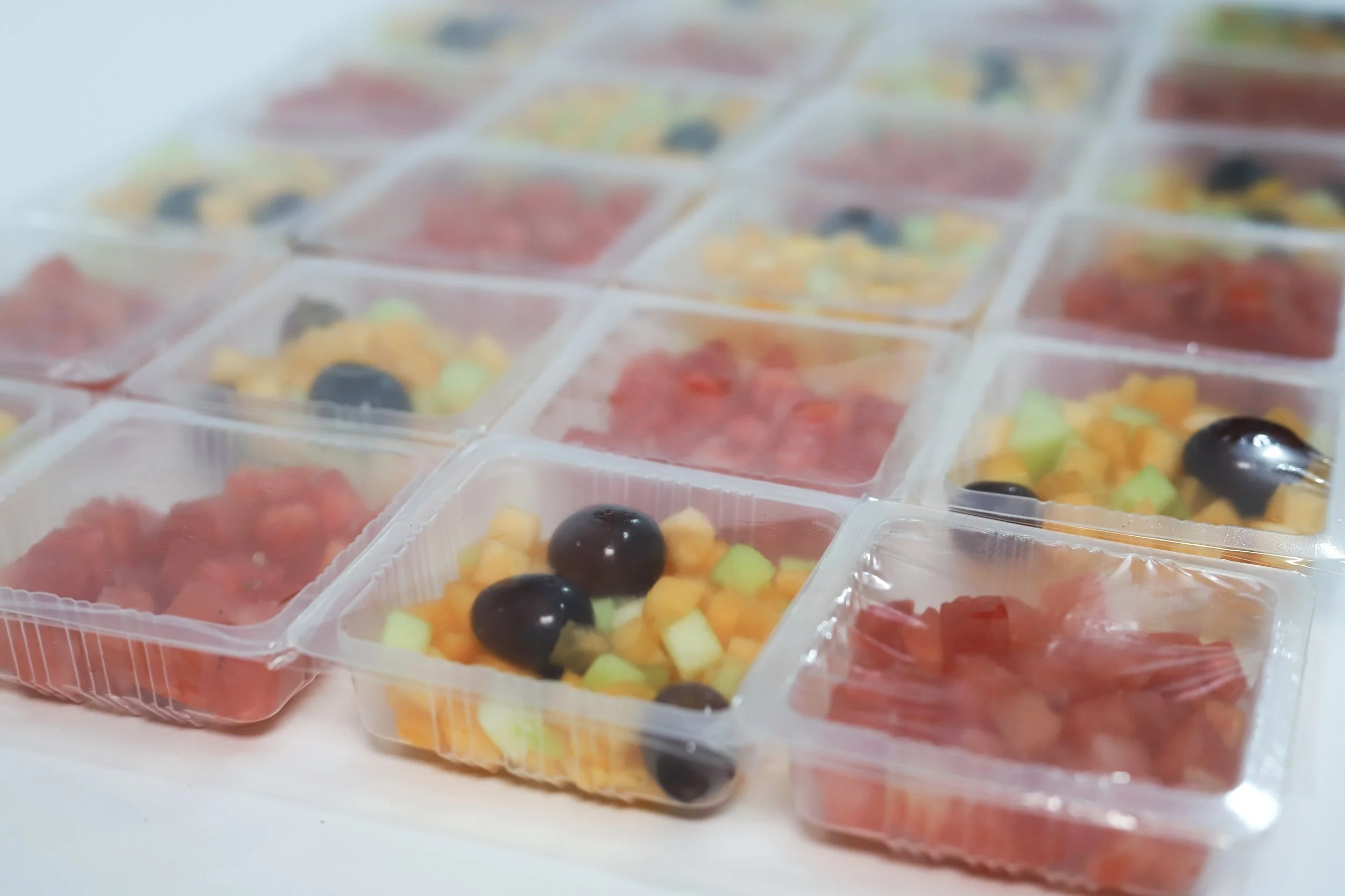 Multiple clear plastic containers filled with colorful miniature food desserts, including fruit toppings and chocolate decorations.