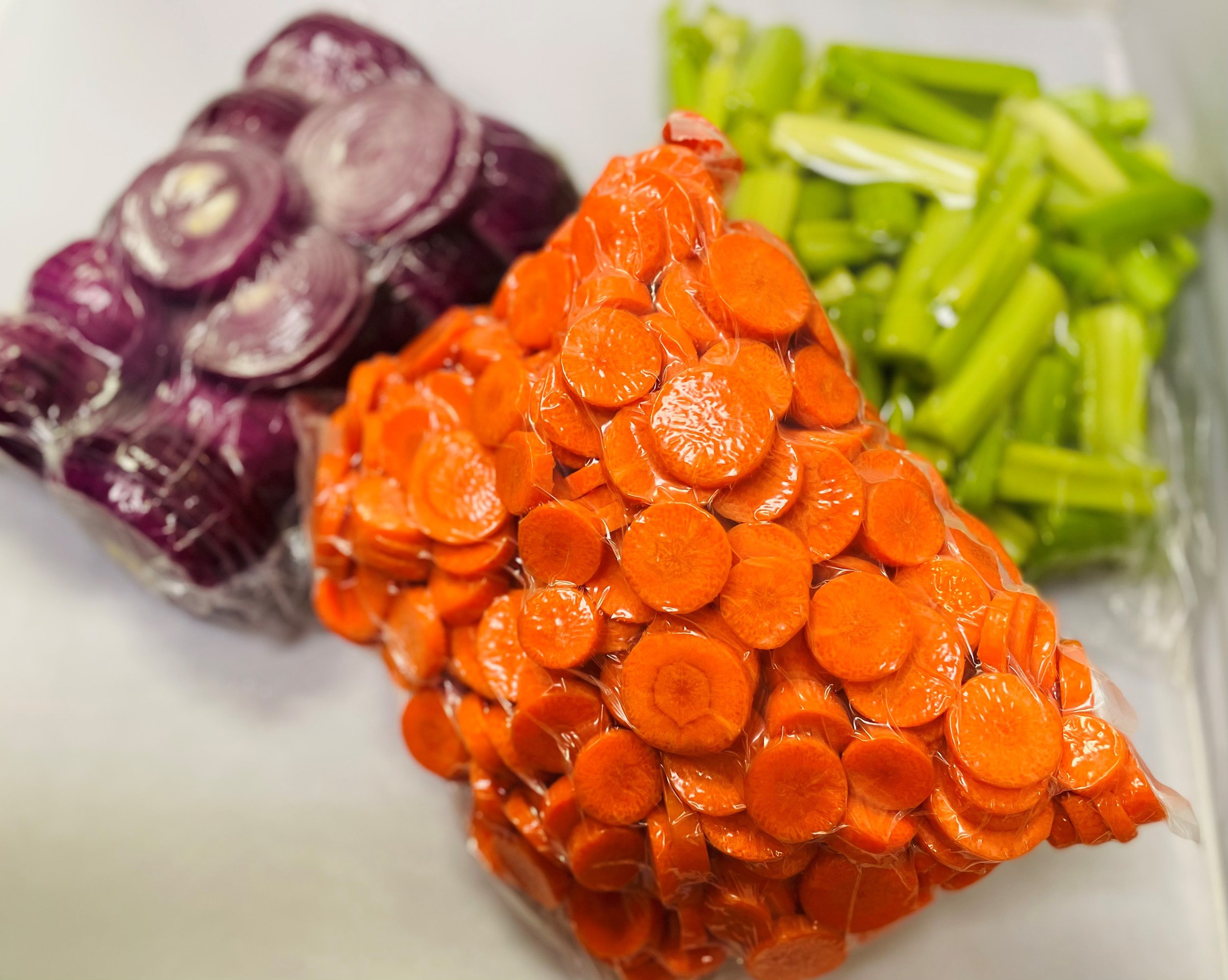 A close-up image of shredded purple beets, orange carrots, and green celery stalks arranged together on a white surface.