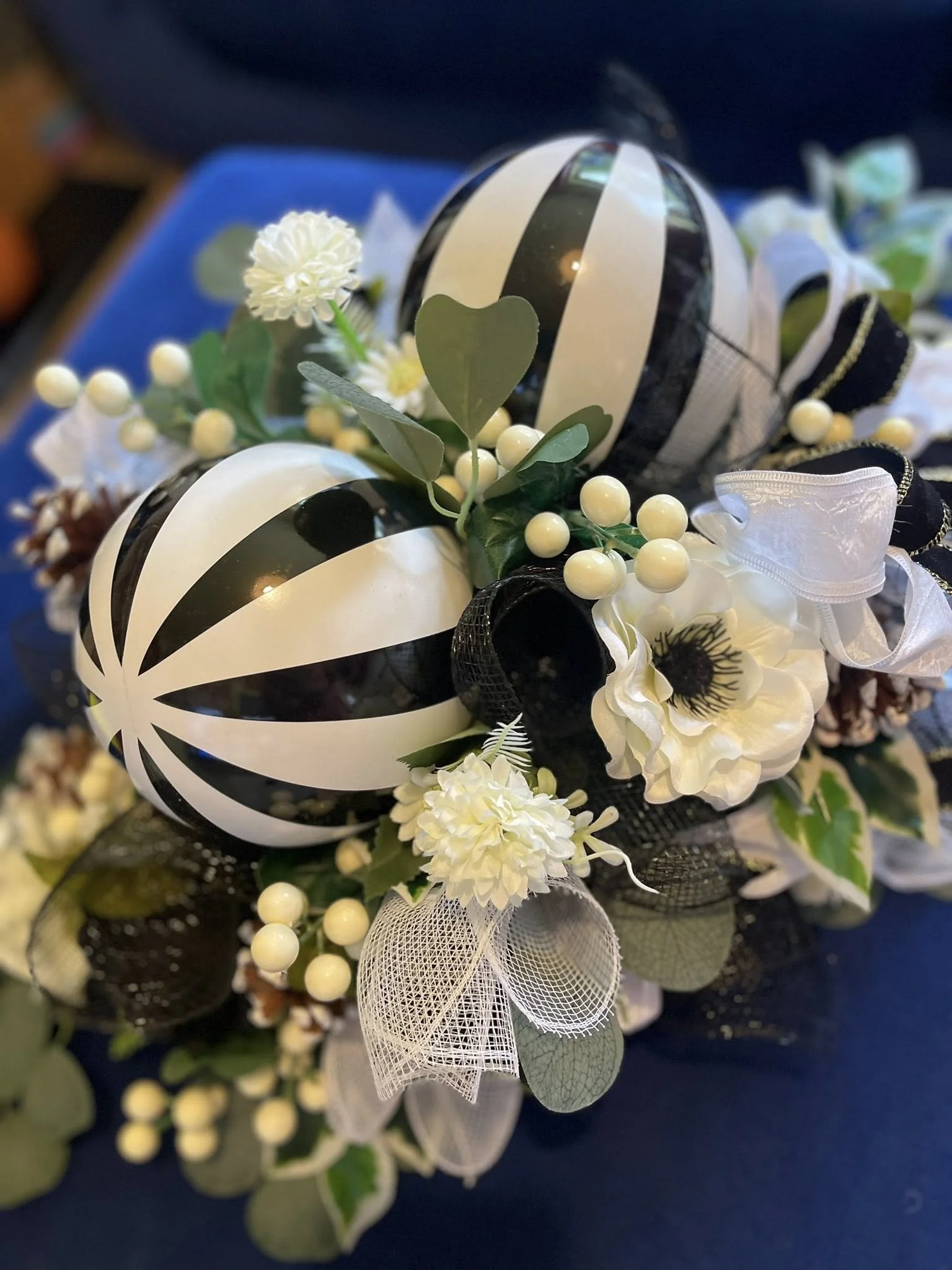 Decorative arrangements with black and white striped balloons, artificial white flowers, green leaves, white berries, and ribbons.