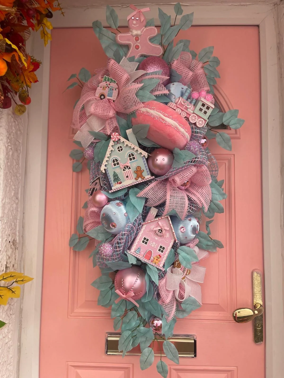 Decorative Christmas wreath on a pink door, featuring pink and blue ornaments, houses, a gingerbread man, and ribbons.