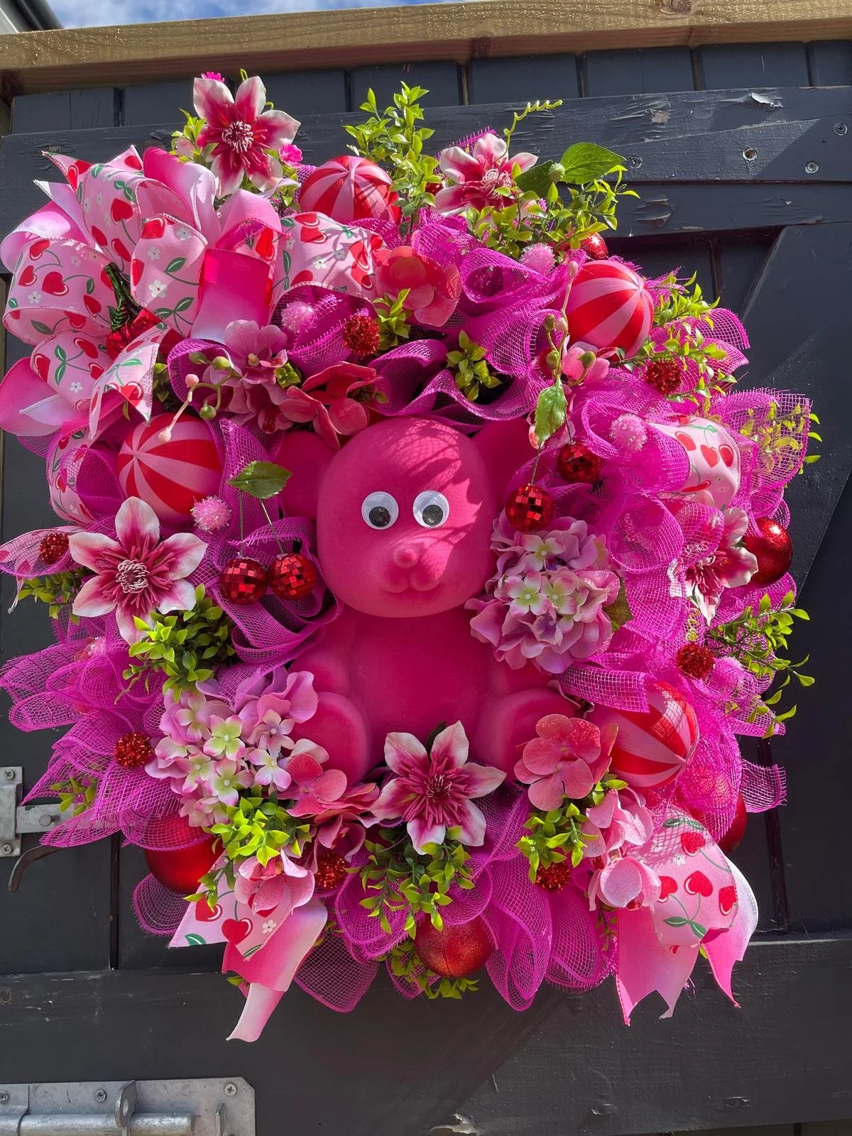 Pink decorative wreath with a stuffed pig, pink flowers, pink ribbon bows, and red ornaments.