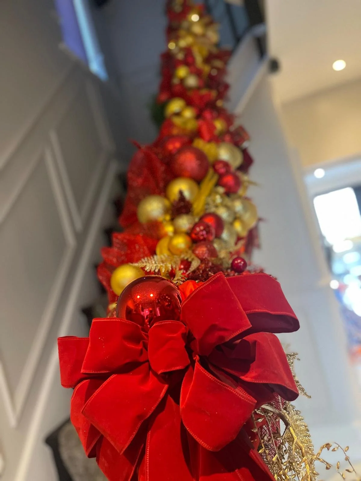 Close-up of a Christmas decoration featuring red and gold ornaments, a large red bow, and festive gold accents on a long garland or centerpiece.