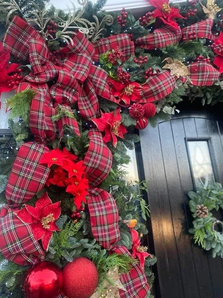 Decorated front door with a Christmas wreath featuring red plaid ribbons, poinsettia flowers, red ornaments, berries, gold accents, and greenery.