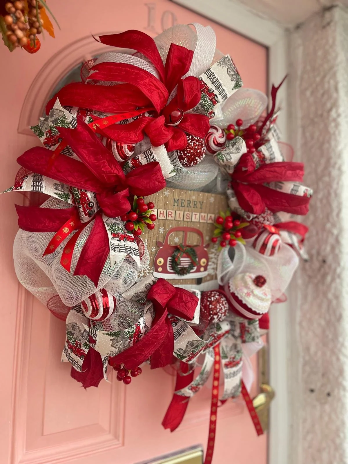 Christmas wreath with red, white, and festive ribbons, berries, and ornaments hanging on a pink door