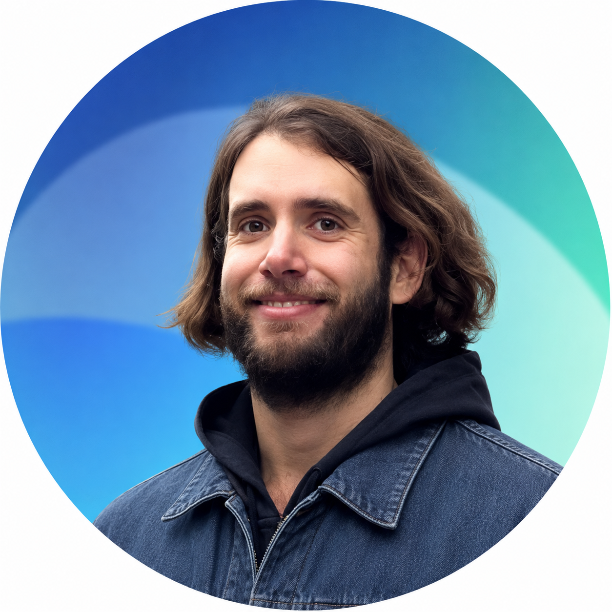 Portrait of a man with medium-length wavy brown hair and a beard, smiling, wearing a dark hoodie and denim jacket, against a blue and green gradient background.