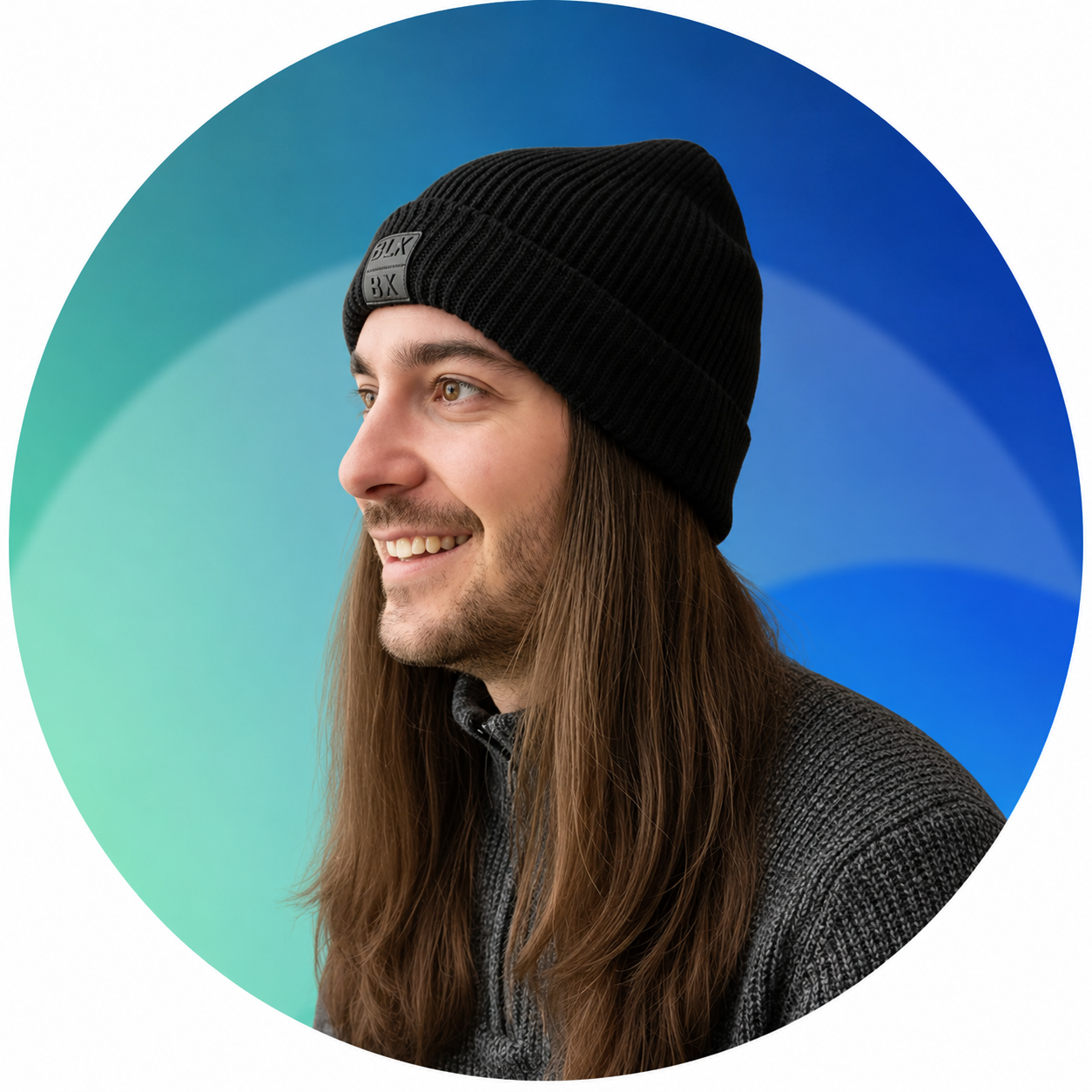 Profile of a smiling man with long hair, wearing a black knit beanie and a gray textured jacket, against a colorful abstract background.