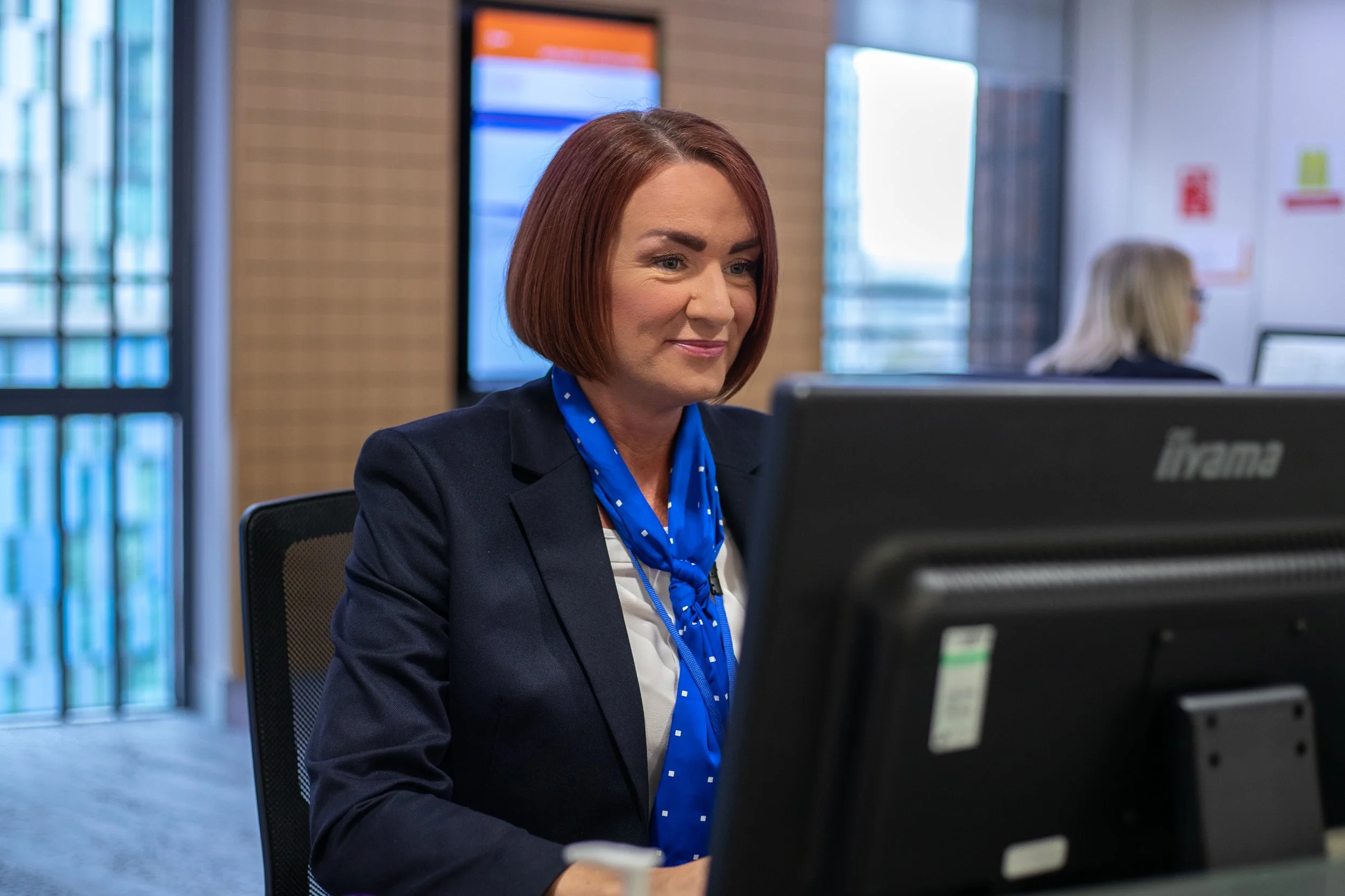 A woman with short red hair working at a computer in a modern office.