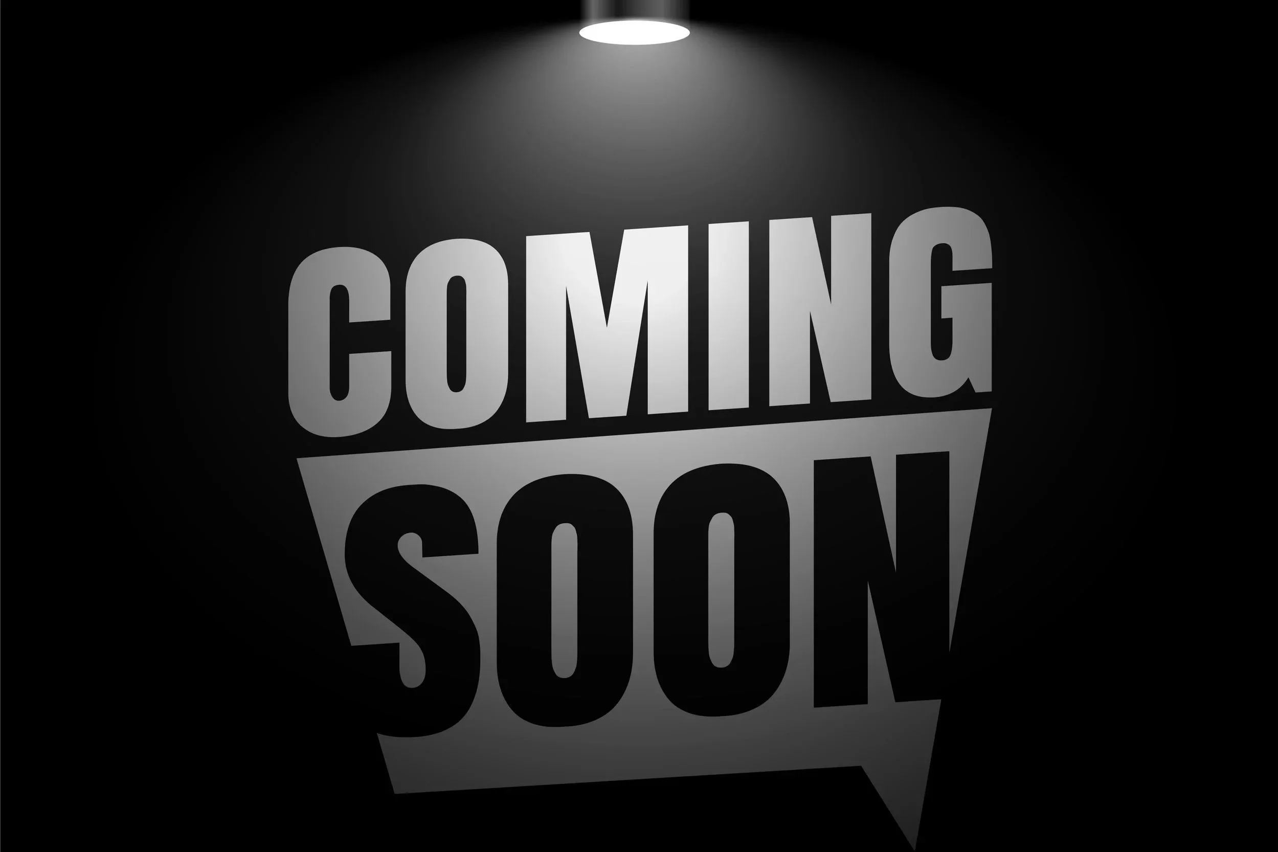 A black background with a spotlight at the top illuminating a speech bubble containing the words 'COMING SOON' in large, bold letters.