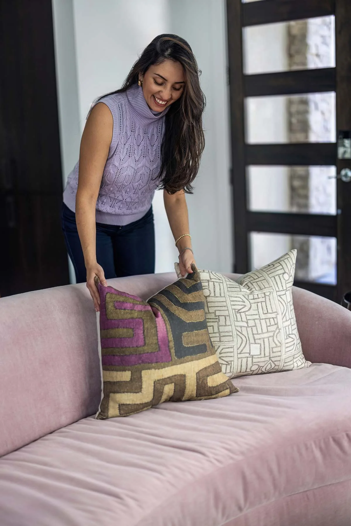 Woman arranging cushions on a pink couch in a modern living room.