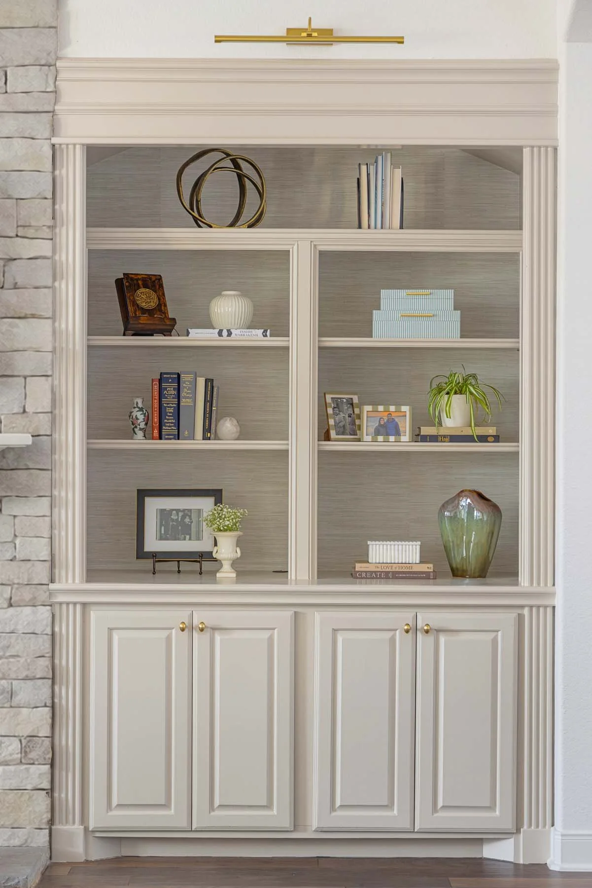A white built-in bookshelf with decorative items and framed photos, against a white wall with brick on the left side.