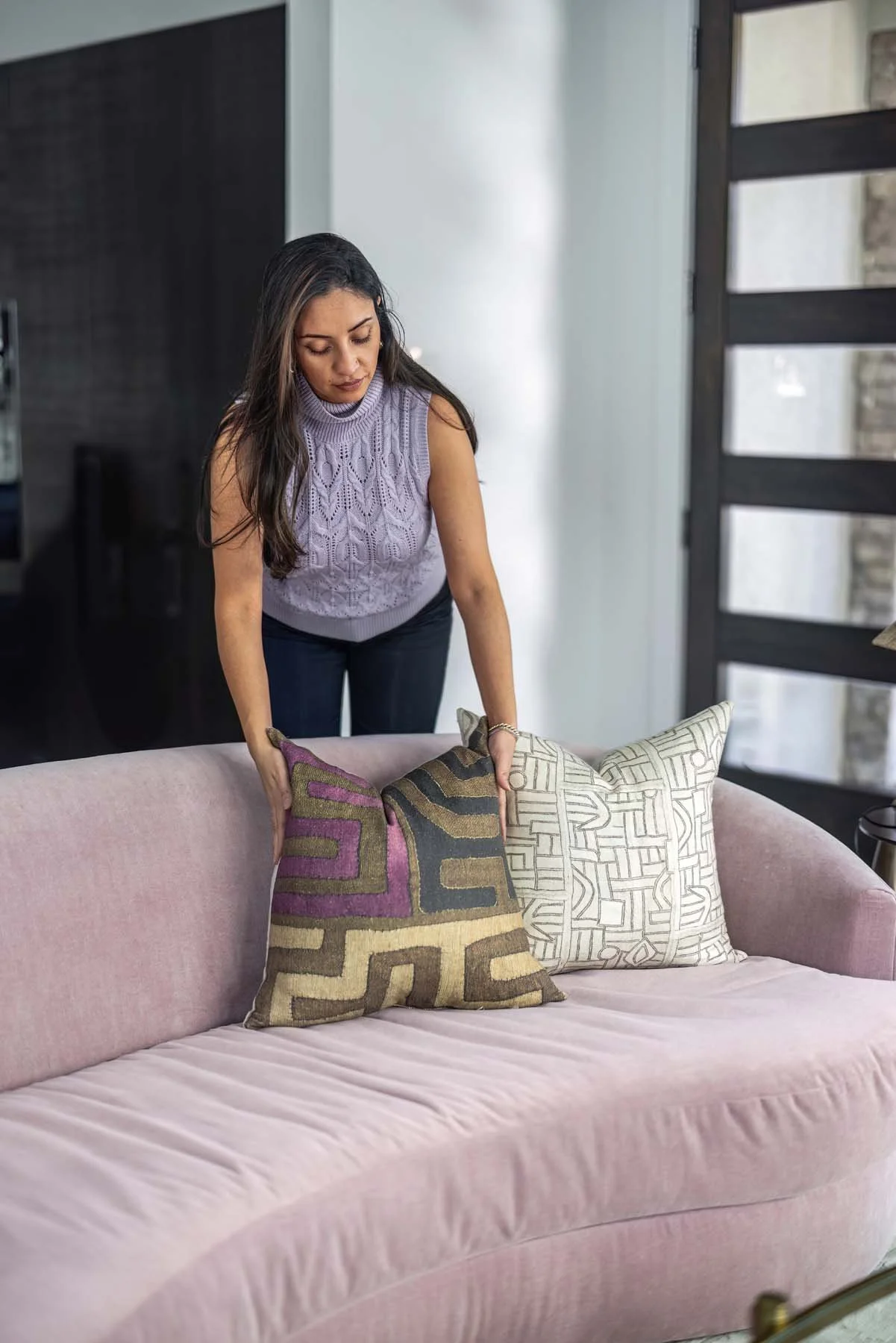 A woman arranging decorative pillows on a pink sofa in a modern living room.