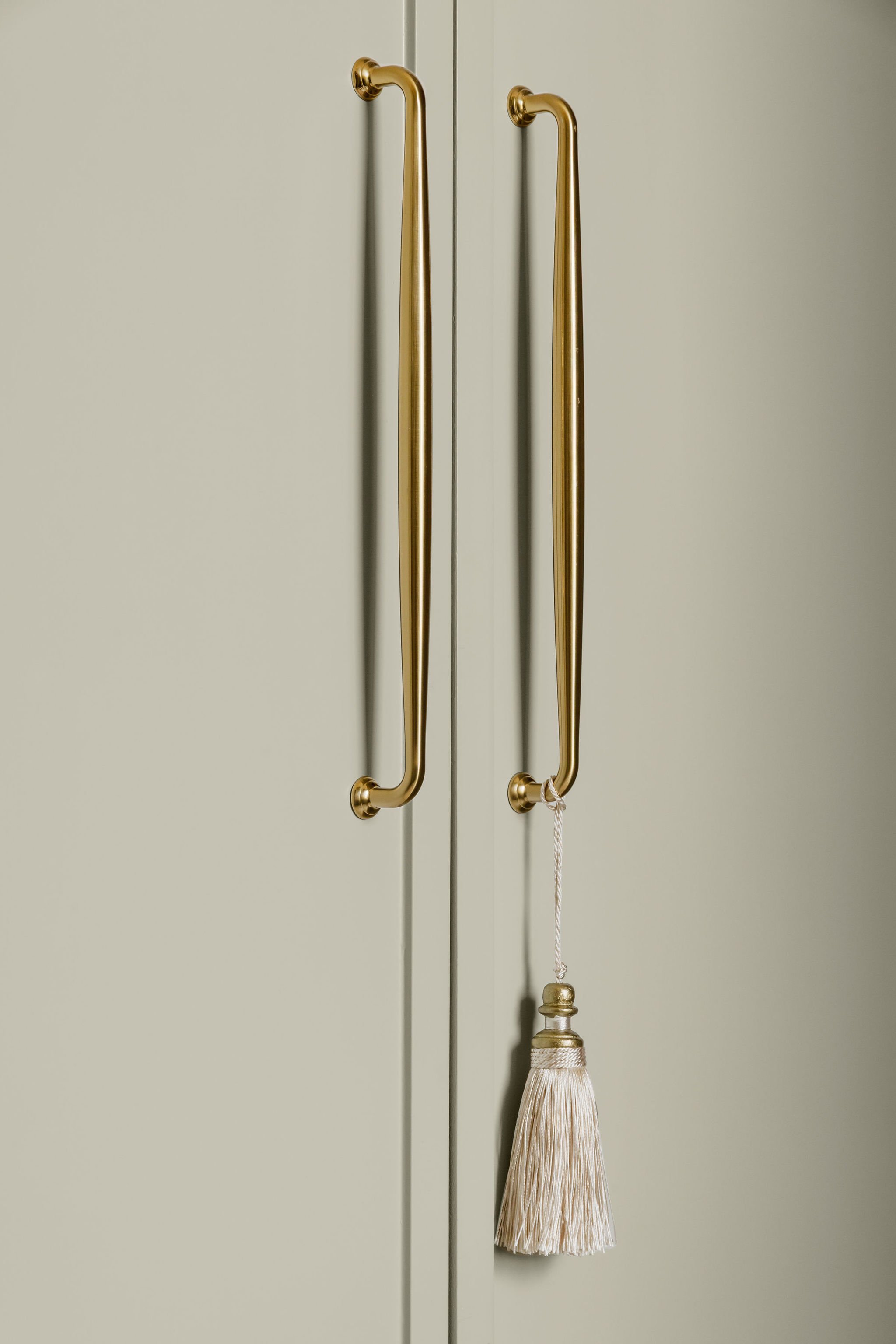A pair of gold-colored door handles on closed light-colored closet doors, with a decorative tassel hanging from one handle.