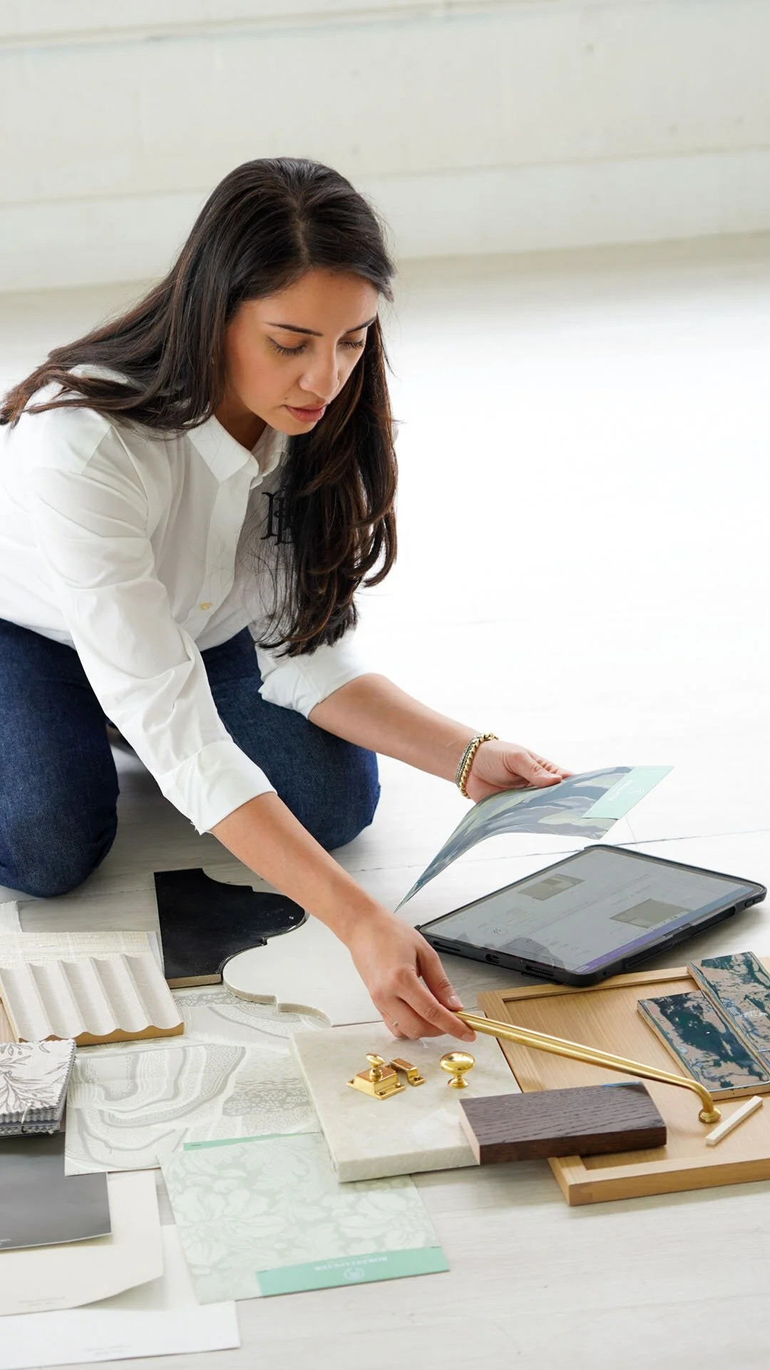 Woman selecting interior design materials including photos, fabric swatches, and decor items on the floor.