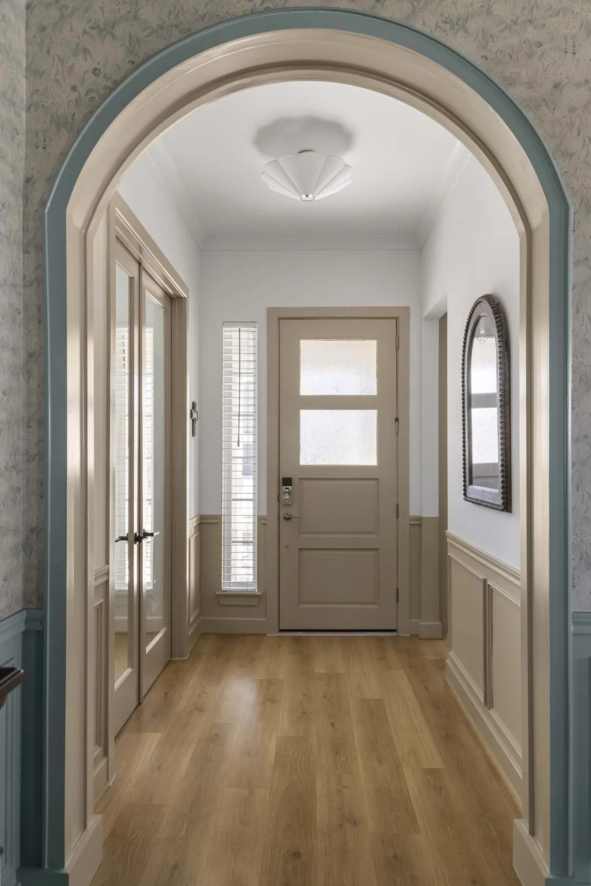 Entrance hallway with a beige door and windows, wood flooring, mirror on the wall, and arched doorway with blue trim.