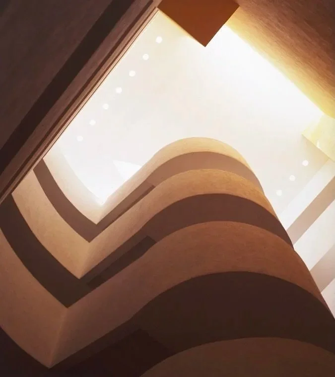 Vista desde abajo de un interior de un edificio con varias terrazas circulares y una iluminación natural que entra por un espacio central abierto.