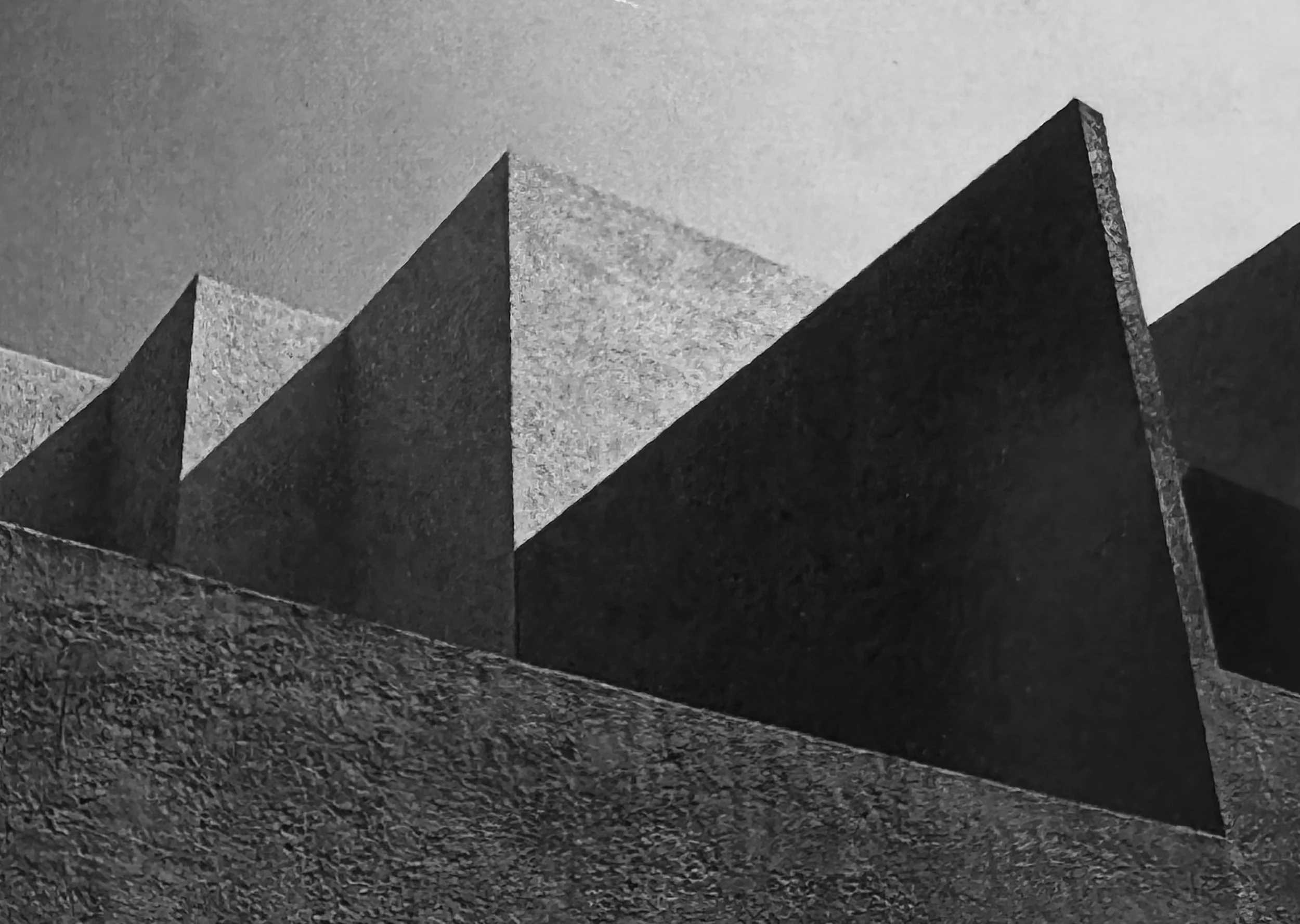 Una escultura de bloques de piedra apilados en forma de picos, en una superficie de tierra con vegetación.