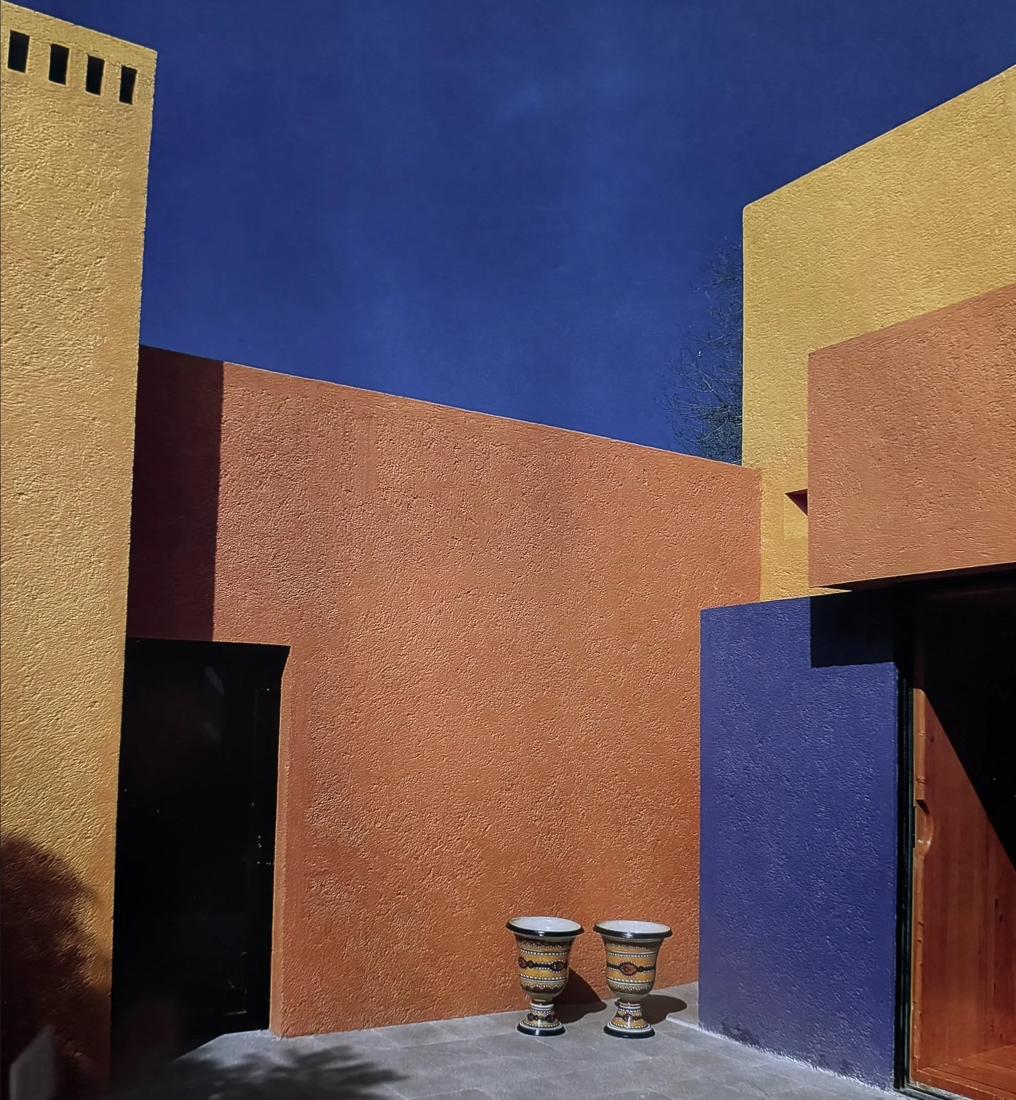 Exterior de un edificio con paredes color amarillo y naranja, decorado con dos jarrones con patrones coloridos en el suelo, bajo un cielo nocturno.