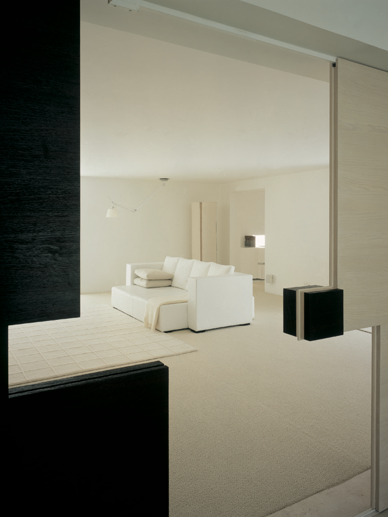 Sala de estar moderna con sofá blanco, alfombra crema, paredes blancas y lámpara de pared ajustable. Eucaliptos 65, Architecture & Design by Rafael Aragonés Caballero & Miguel Ángel Aragonés | Taller Aragonés. Photo by Nicola Lorusso