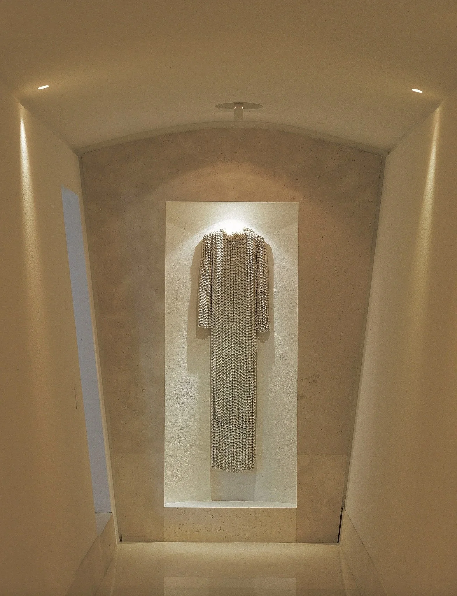 Estatua de una mujer con vestido largo y decorativo, en una galería de arte con paredes de color beige y piso de mármol.