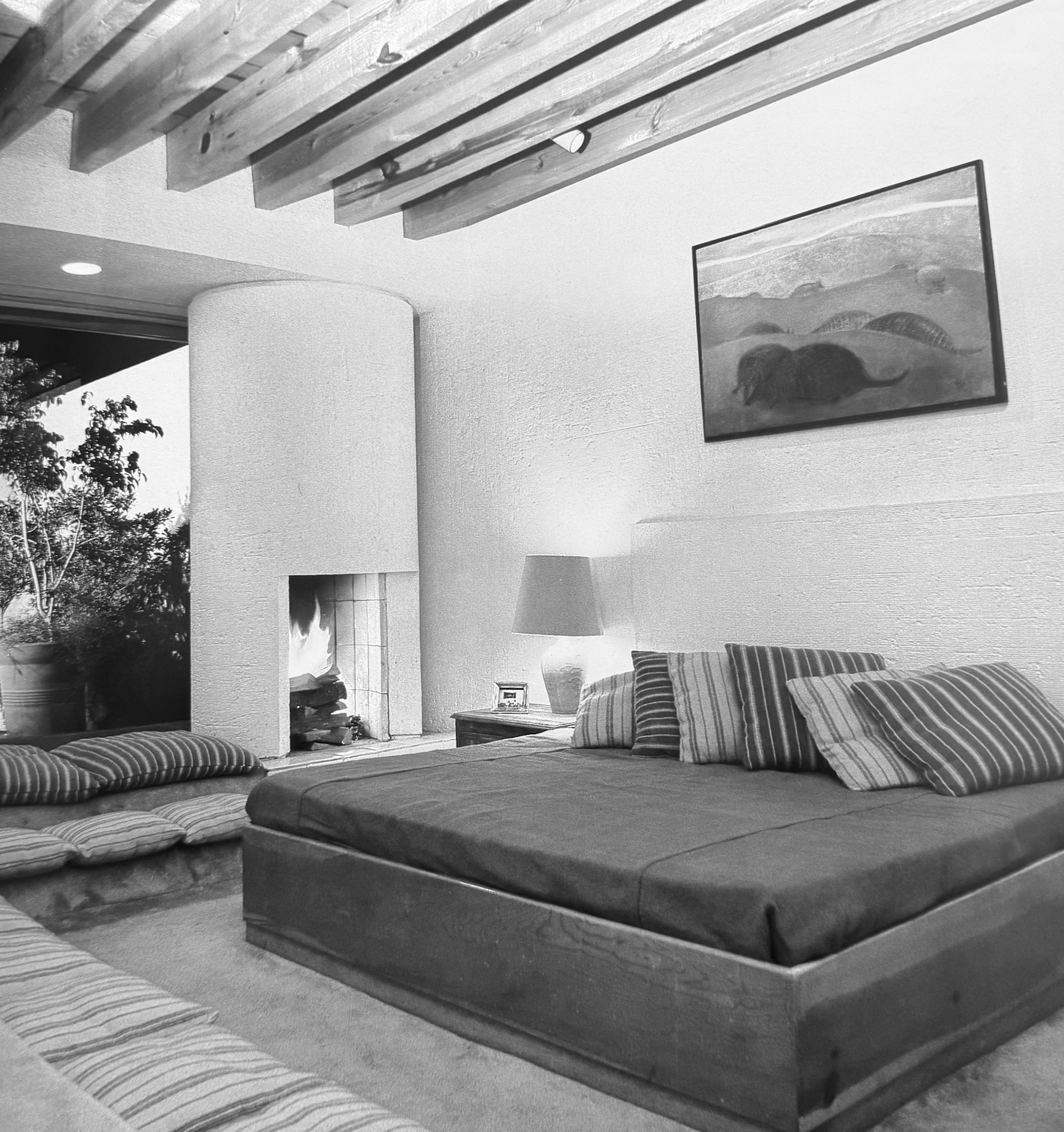 Sala de estar con sillones de cojines a rayas y mesa de centro de madera, cuadro en la pared, paredes blancas y techo con vigas de madera.