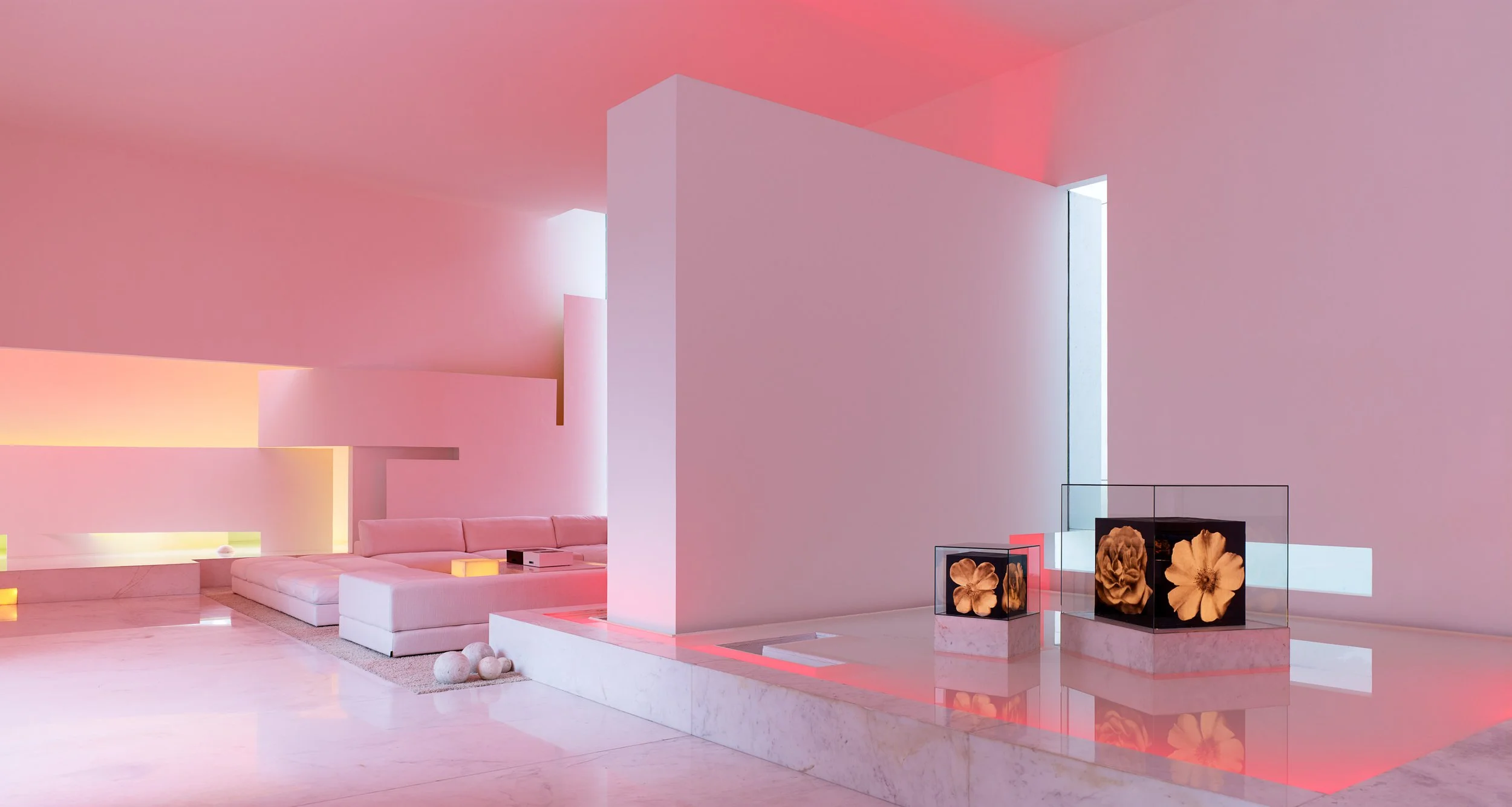 Interior moderno con paredes rosas, iluminación suave y muebles blancos, incluyendo un sofá y exhibiciones con flores.