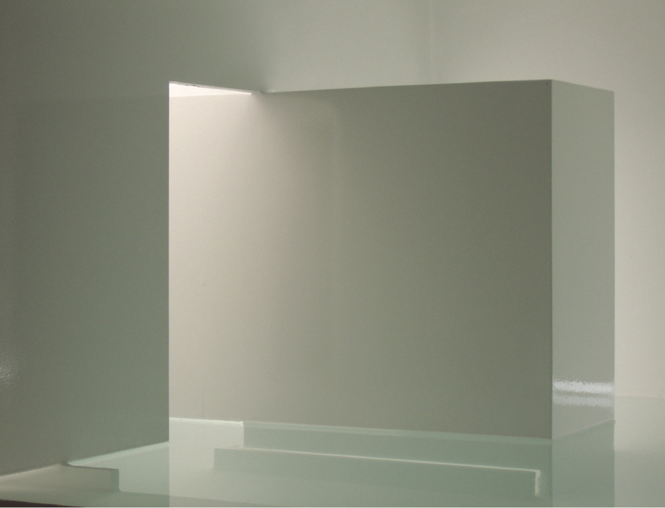 Espacio minimalista con paredes y estructura en color gris claro y luz natural entrando por una abertura en la pared.