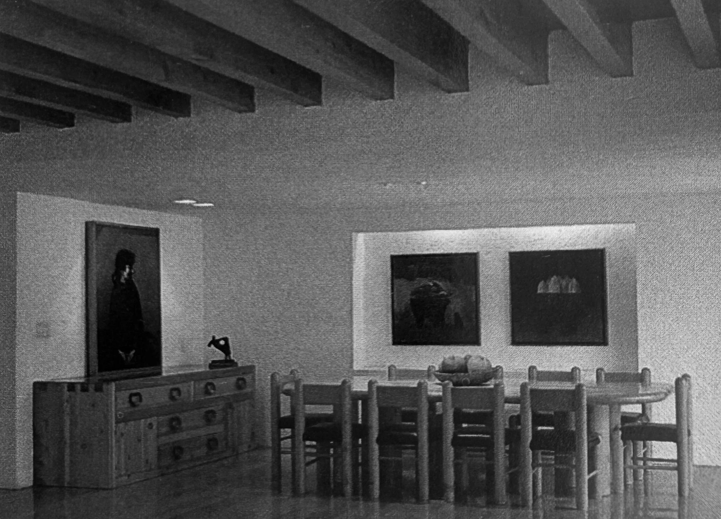 Interior de una sala de juegos para niños con sillas de madera y un árbol de bloques de juguete en primer plano, paredes decoradas con cuadros y ventanas.