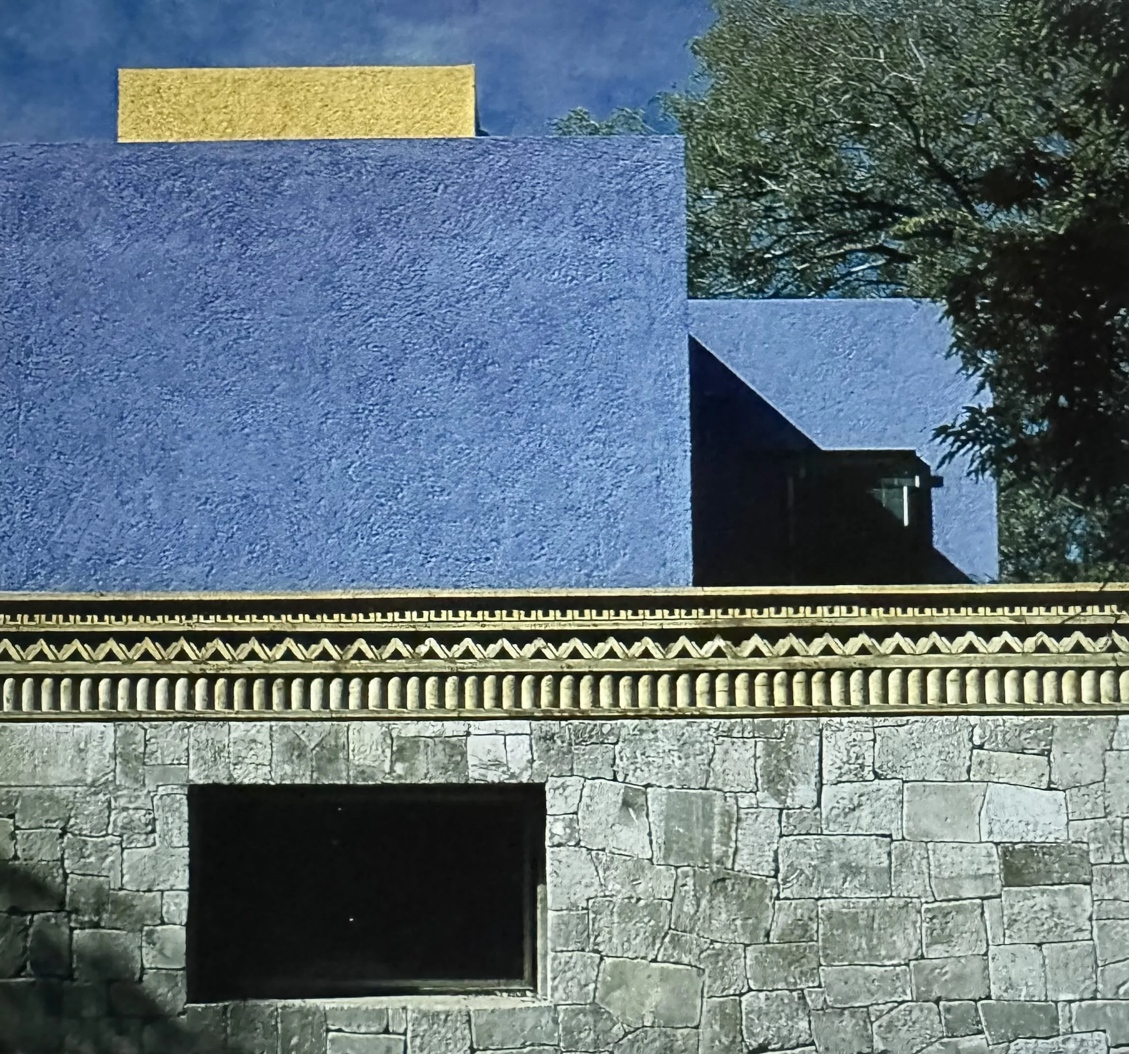 Vista de un muro de piedra con diferentes texturas y colores, adornado con una reja en la parte inferior y rodeado de árboles y cielo en el fondo.