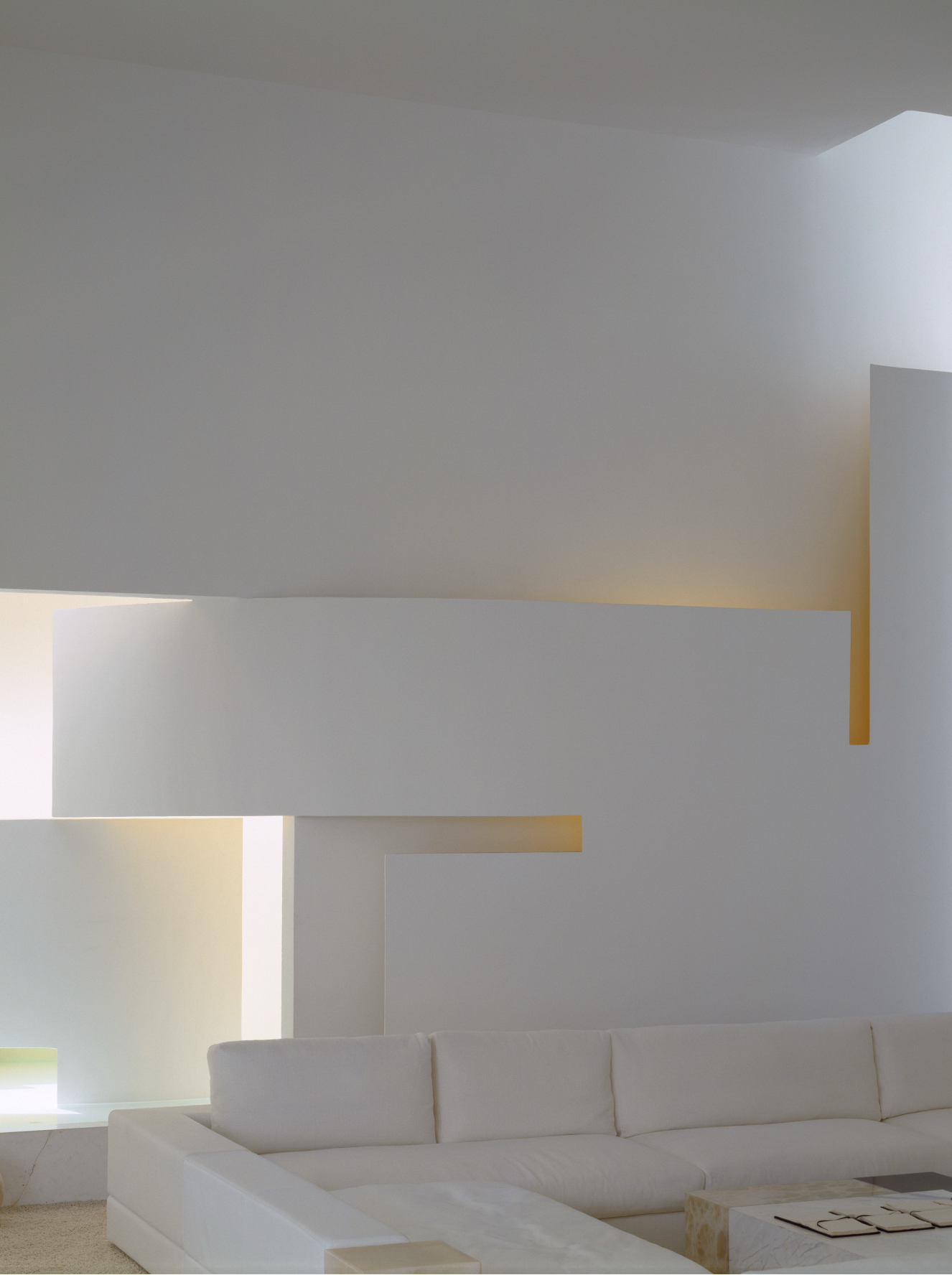 Salón moderno con paredes blancas, techo y muebles blancos, ventanas grandes con luz natural y una mesa de centro de mármol.