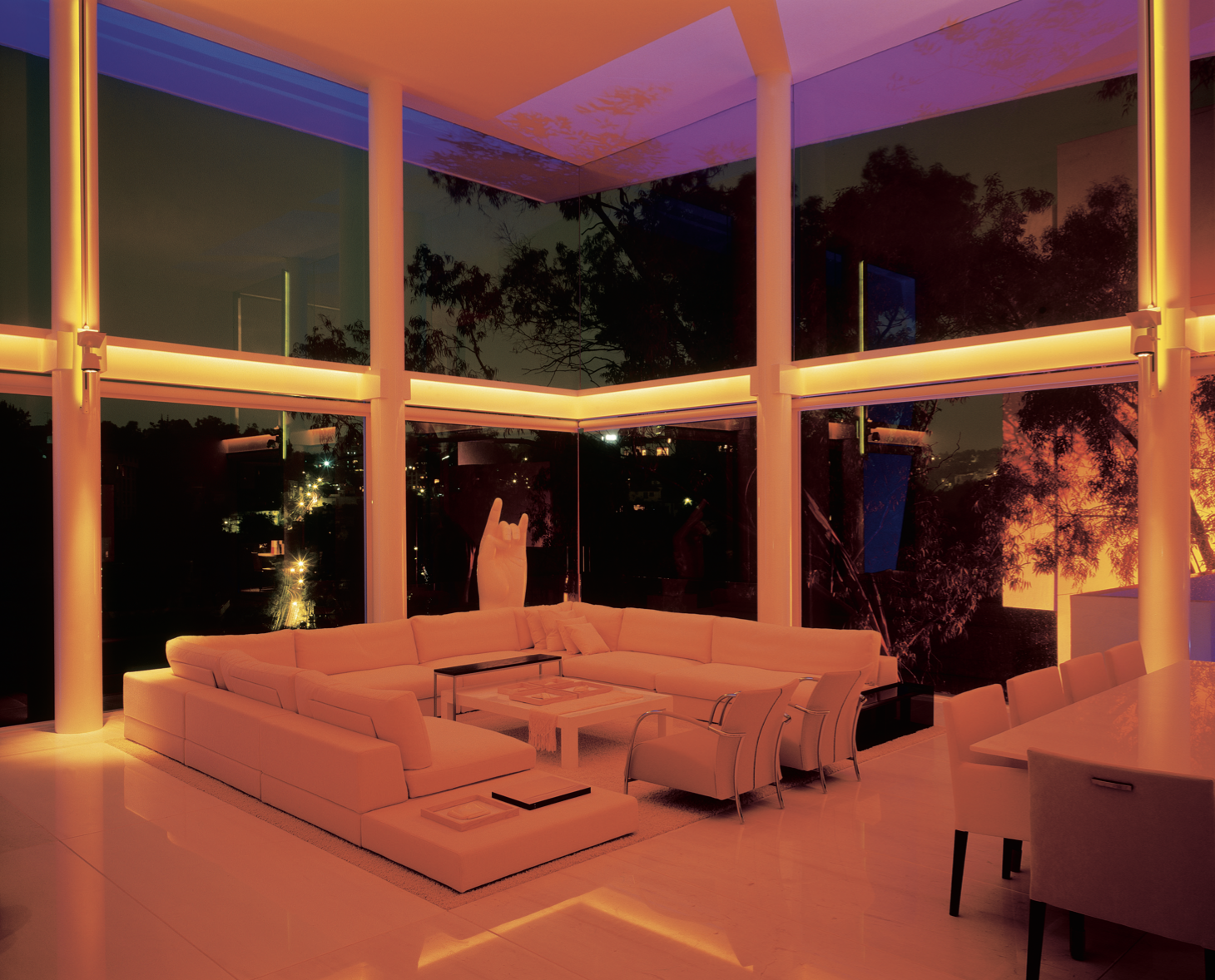 Sala moderna con iluminación de neón naranja y grandes ventanas de vidrio, con vista a la noche y árboles afuera.