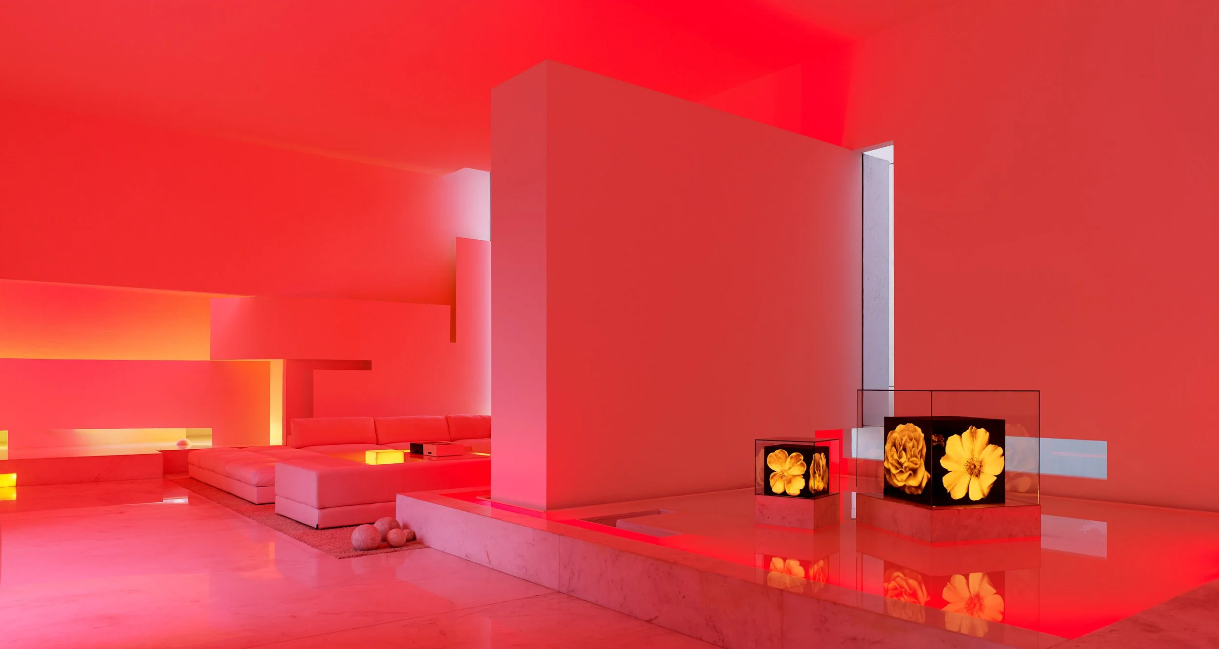Interior moderno con paredes y techo en tonos rojos, mobiliario blanco, pantallas con flores, iluminación suave y decorativa.