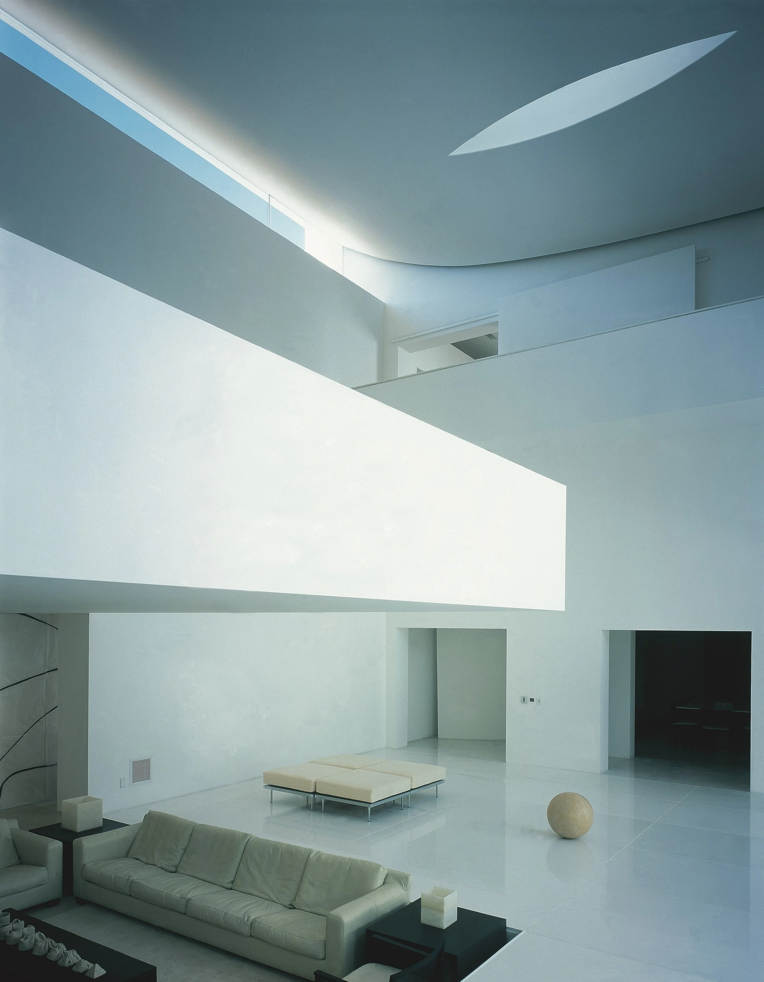 Sala moderna con muebles blancos, sillones y una mesa pequeña, decorada en estilo minimalista y despejada, con paredes blancas y un piso brillante.