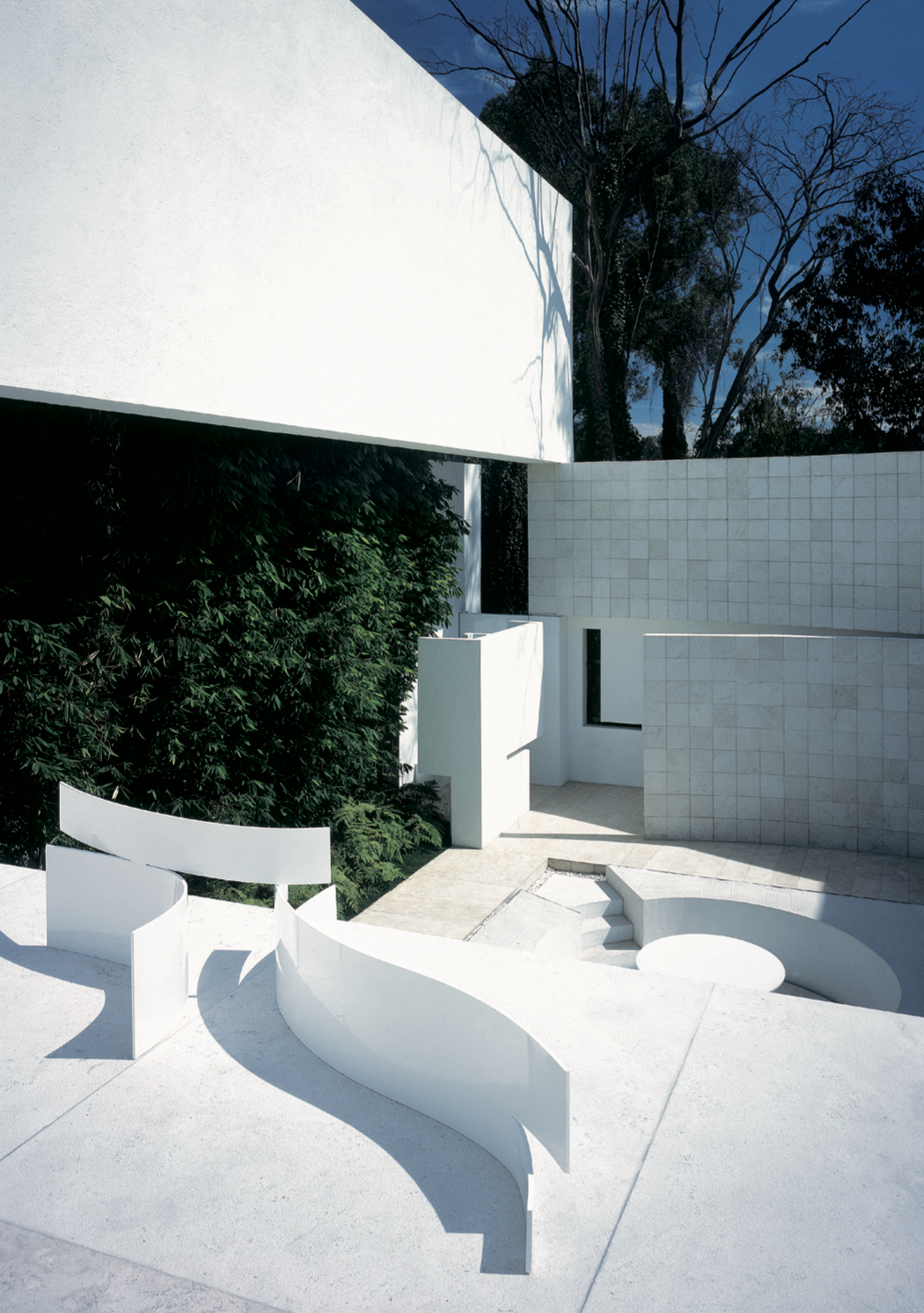 Vista moderna de un edificio blanco con estructuras curvadas y rectas, rodeado de árboles y vegetación, con cielo azul. Eucaliptos 65, Architecture & Design by Rafael Aragonés Caballero & Miguel Ángel Aragonés | Taller Aragonés. Photo by Nicola Lorus