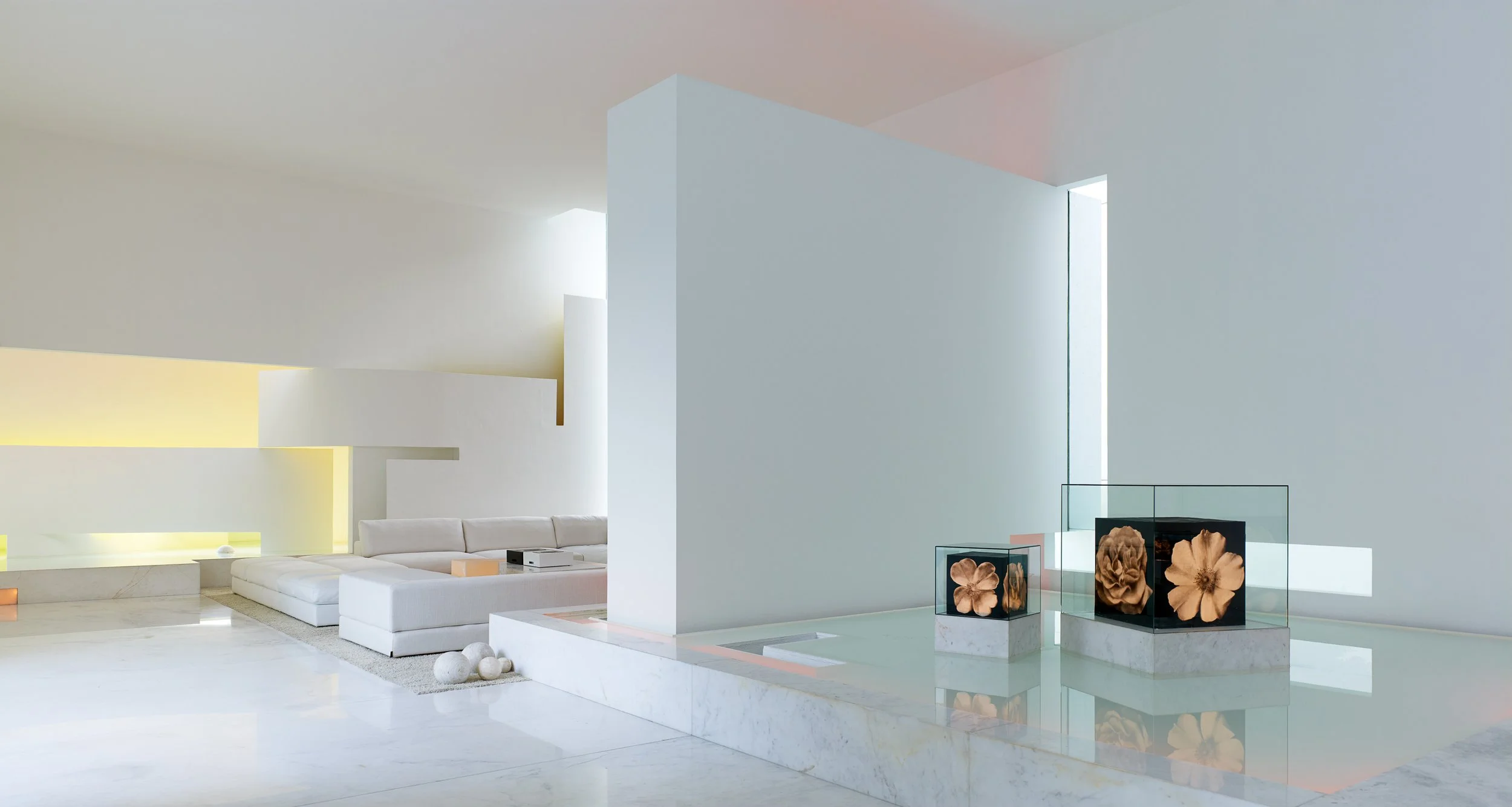 Interior moderno con paredes blancas, zona de descanso con sofá blanco, y exhibiciones de arte con figuras de flores en vitrinas de cristal. Architecture & Design by Miguel Ángel Aragonés | Taller Aragonés. Photography by Joe Fletcher