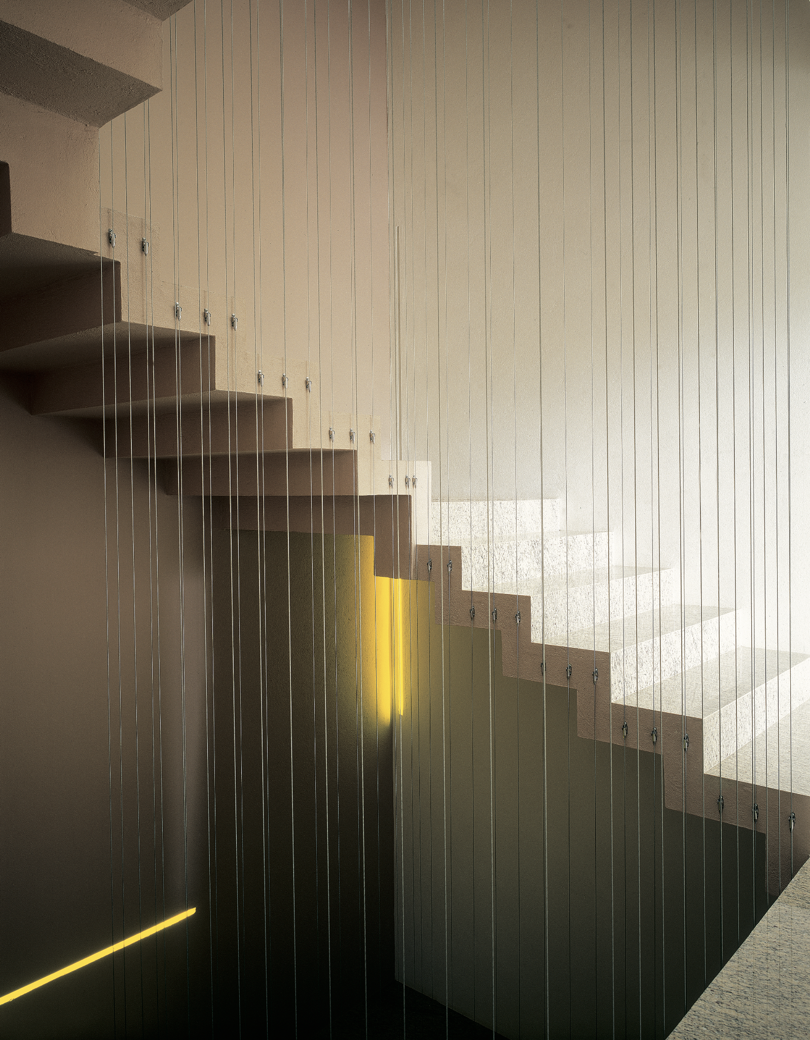 Escalera moderna con barandilla de cables de acero y iluminación en línea amarilla, en un espacio arquitectónico interior.