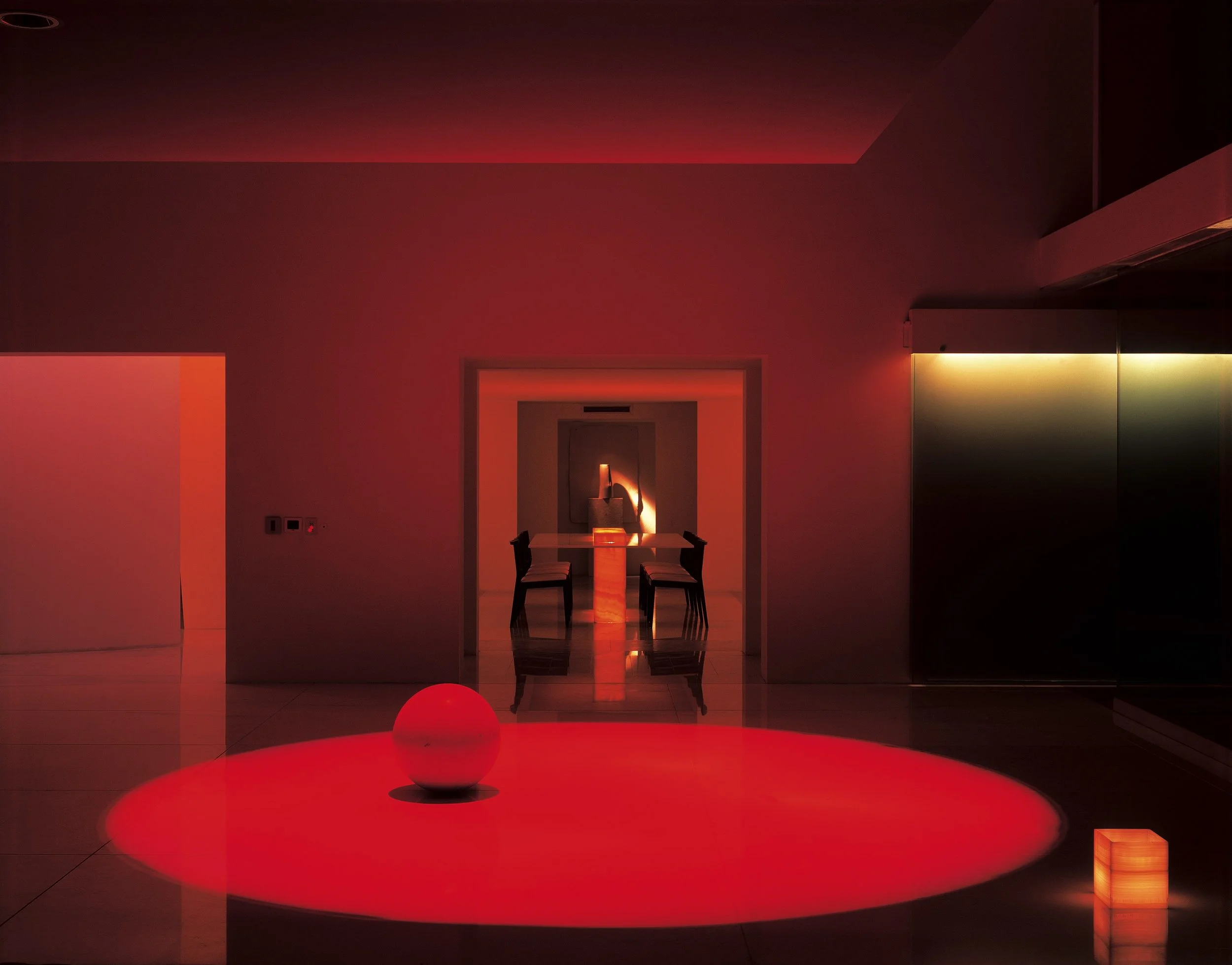 Sala de estar con iluminación ambiental roja, mesa con bola decorativa en el centro, comedor con sillas y paredes de colores cálidos. Eucaliptos 65, Architecture & Design by Rafael Aragonés Caballero & Miguel Ángel Aragonés | Taller Aragonés. Photo b