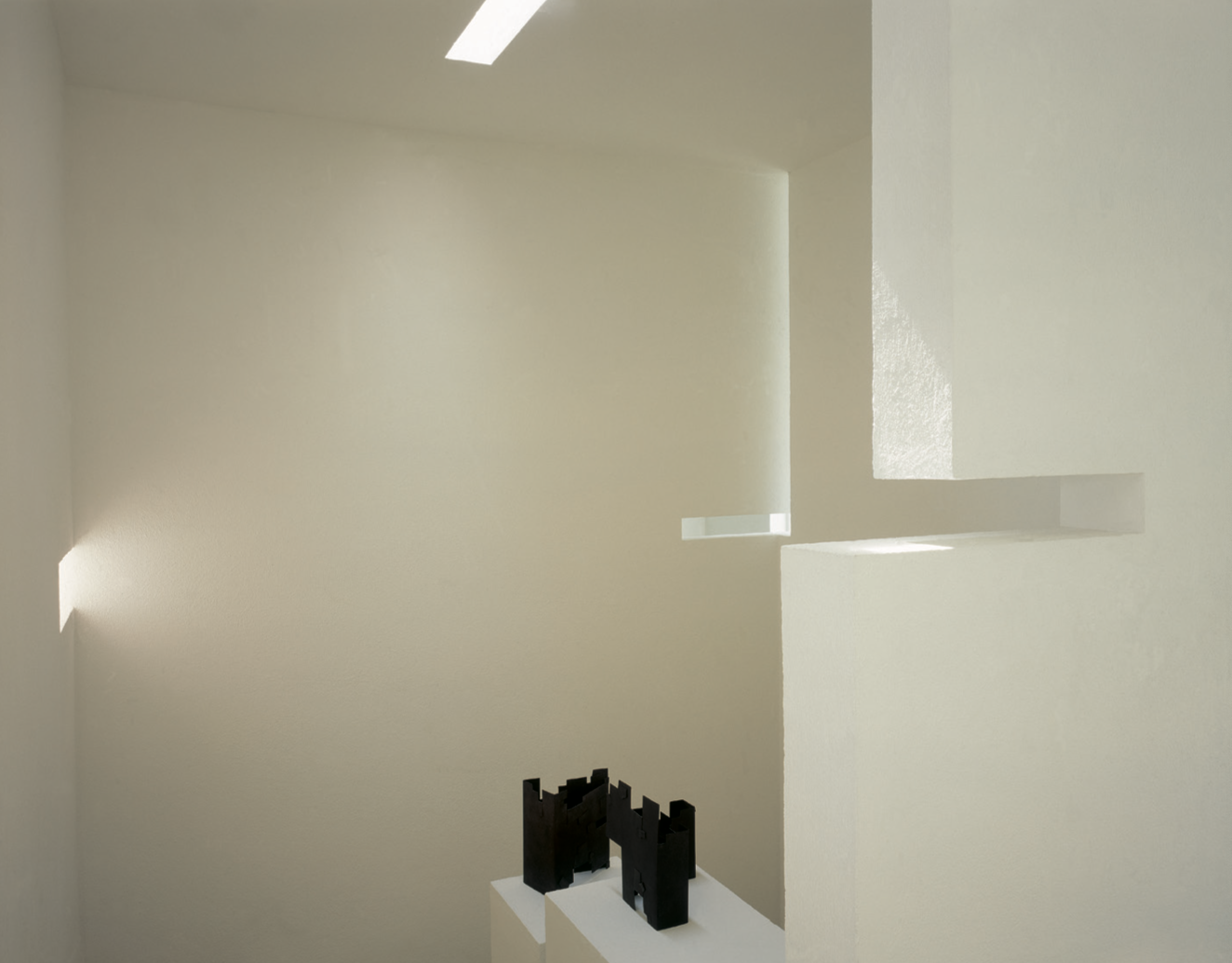 Escultura negra en una sala blanca con ventanas y luz natural.