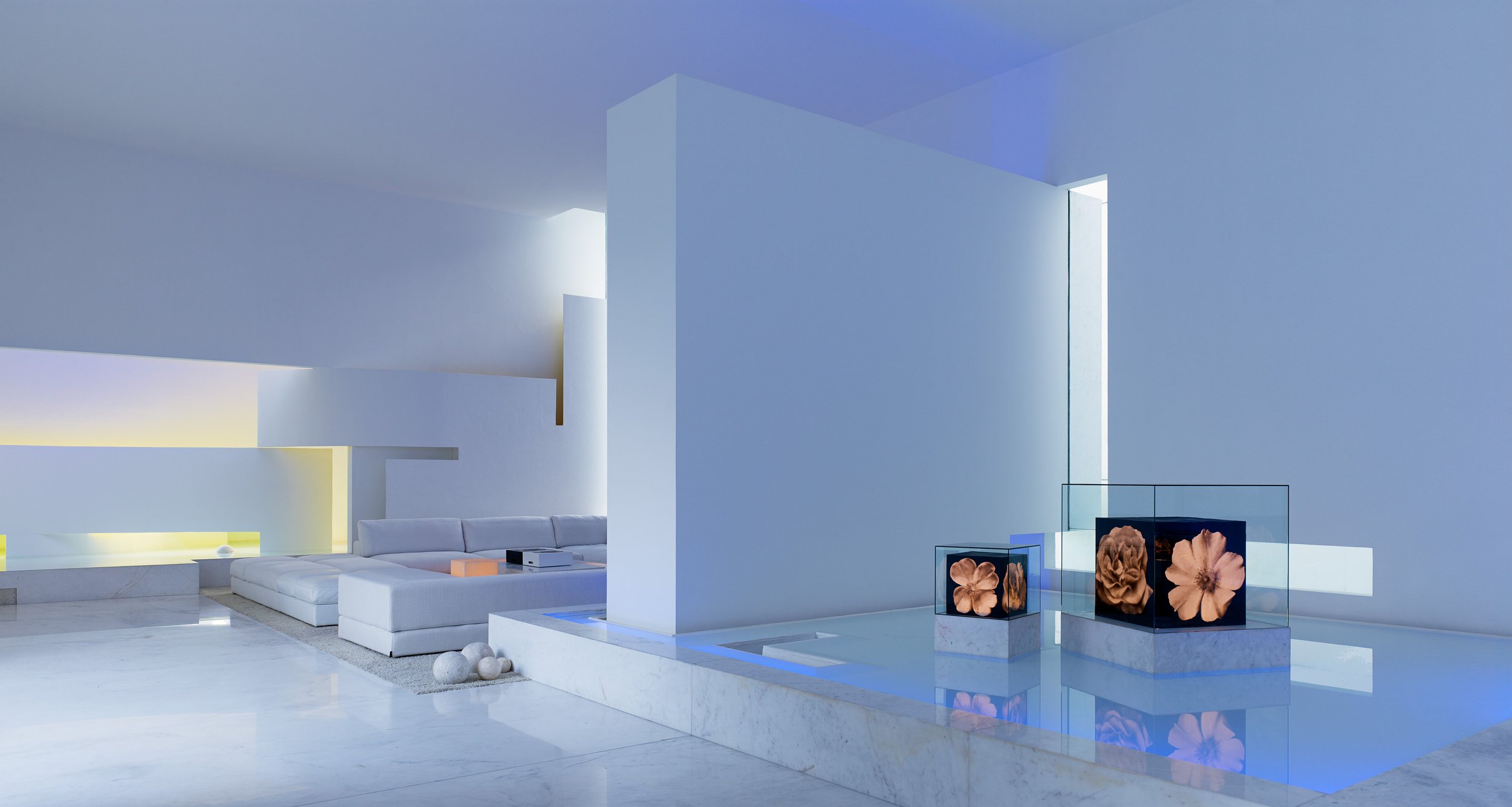 Interior minimalista con paredes blancas, muebles blancos, esculturas de flores en exhibición, y una iluminación suave.
