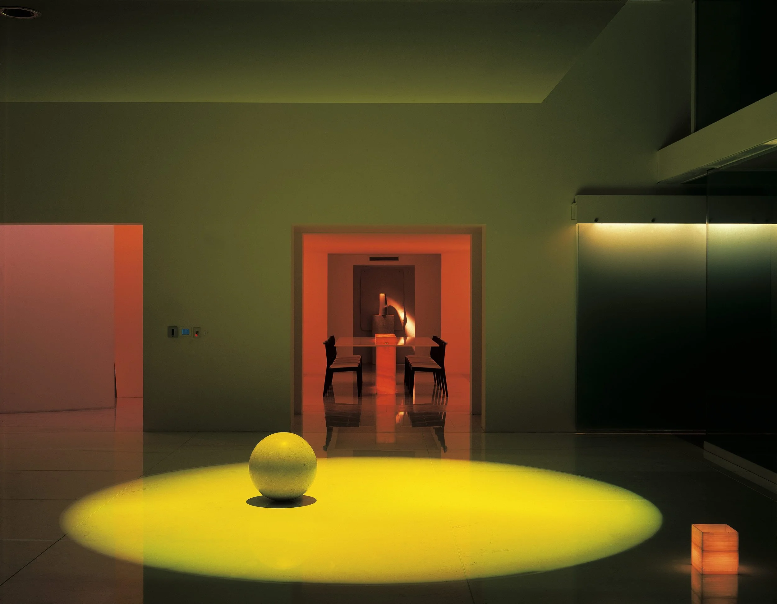 Sala moderna con iluminación ambiental de colores cálidos y fríos, mesa con sillas en el fondo, bola decorativa en el suelo y pared con diseño minimalista. Eucaliptos 65, Architecture & Design by Rafael Aragonés Caballero & Miguel Ángel Aragonés | Ta