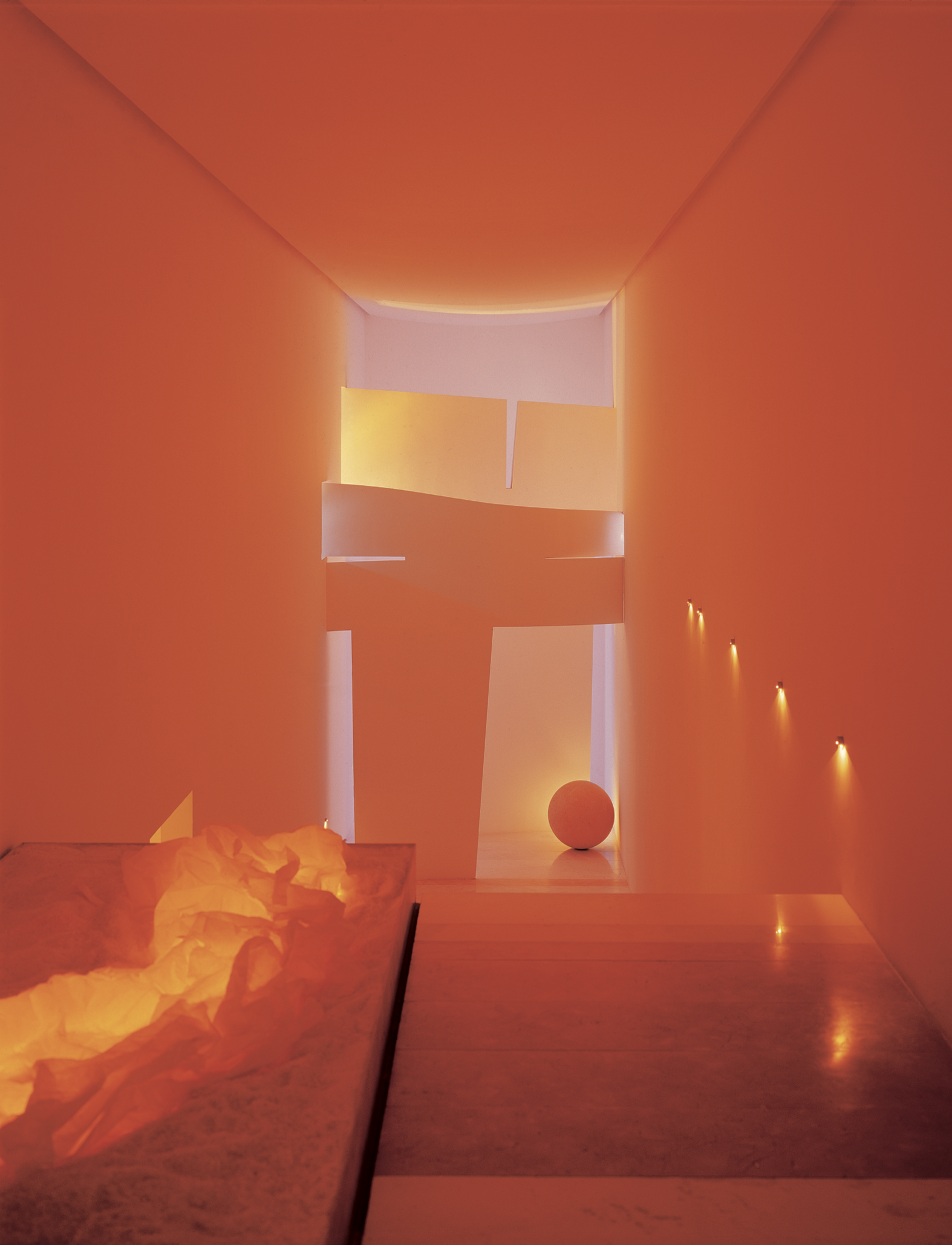 Pasillo interior con paredes y techo en tonos anaranjados, con luz cálida y un balón en el suelo al fondo, además de papel triturado en una caja a la izquierda. Eucaliptos 65, Architecture & Design by Rafael Aragonés Caballero & Miguel Ángel Aragonés