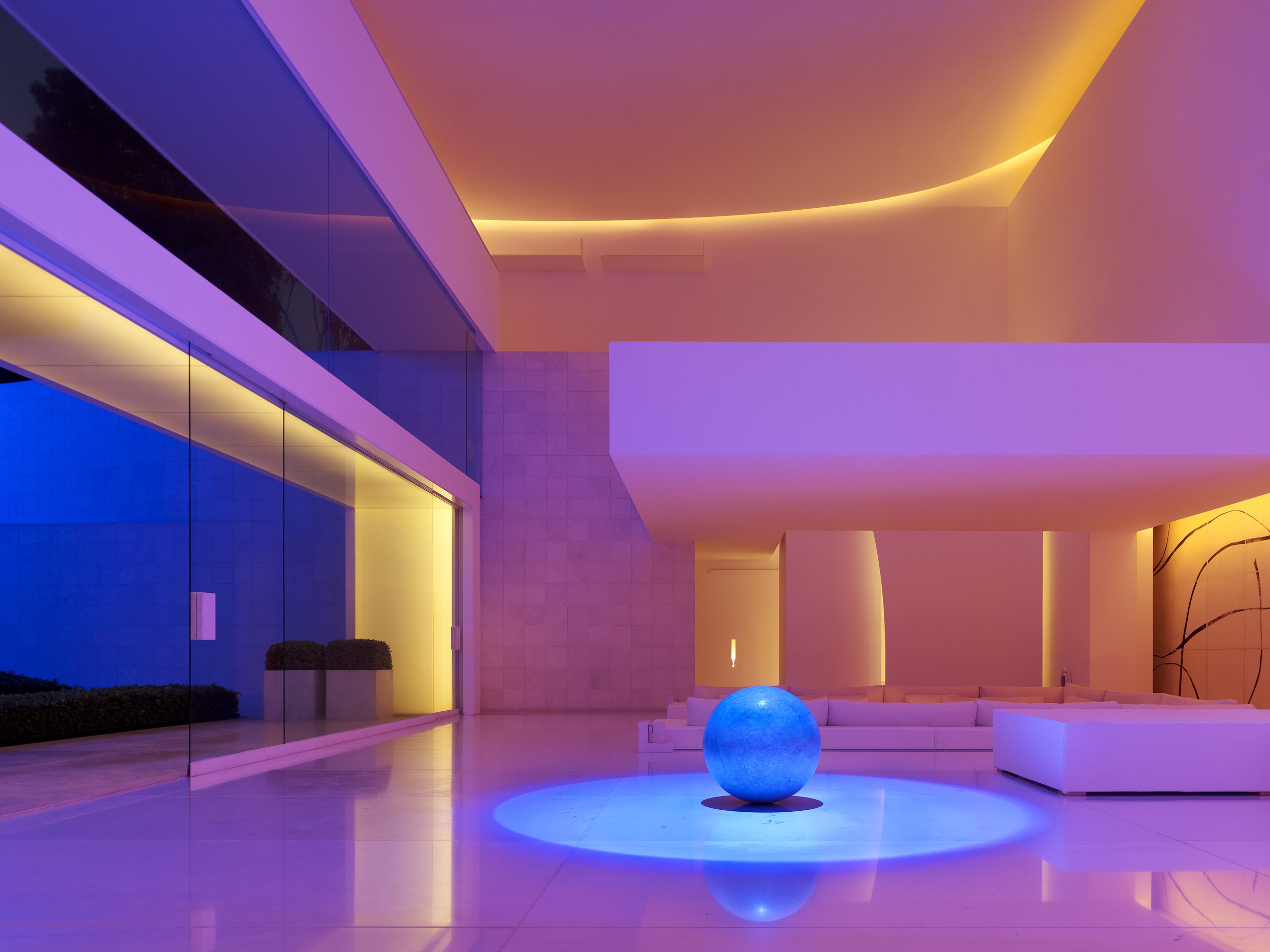 Interior moderno con iluminación de colores vibrantes, sillas blancas, una bola luminosa azul y un diseño minimalista. Eucaliptos 65 (2004). Designed by  Miguel Ángel Aragonés. A study in geometric volumes and natural light. Mexican modernism and emo